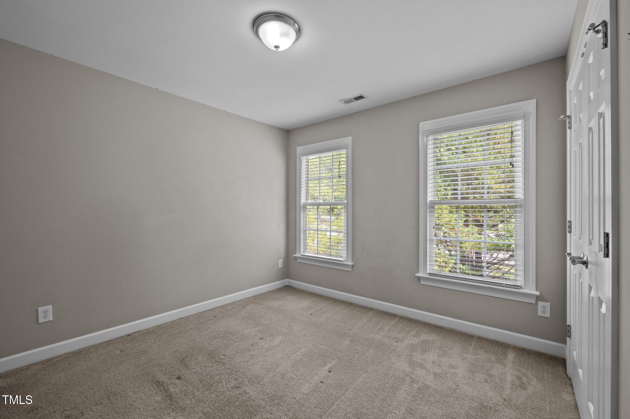 Empty carpeted room with two windows and white blinds.