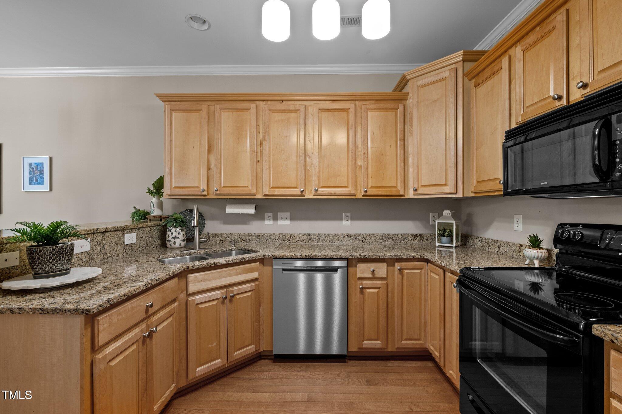 Kitchen with honey-colored wood cabinets, granite counters, stainless dishwasher, and black range and microwave.