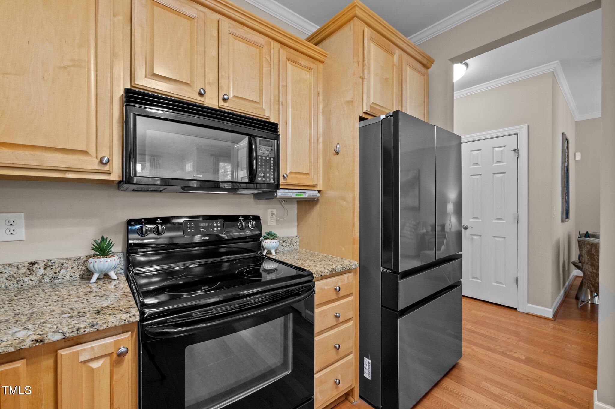 Kitchen with light wood cabinets, granite counters, black appliances, and hardwood floors.