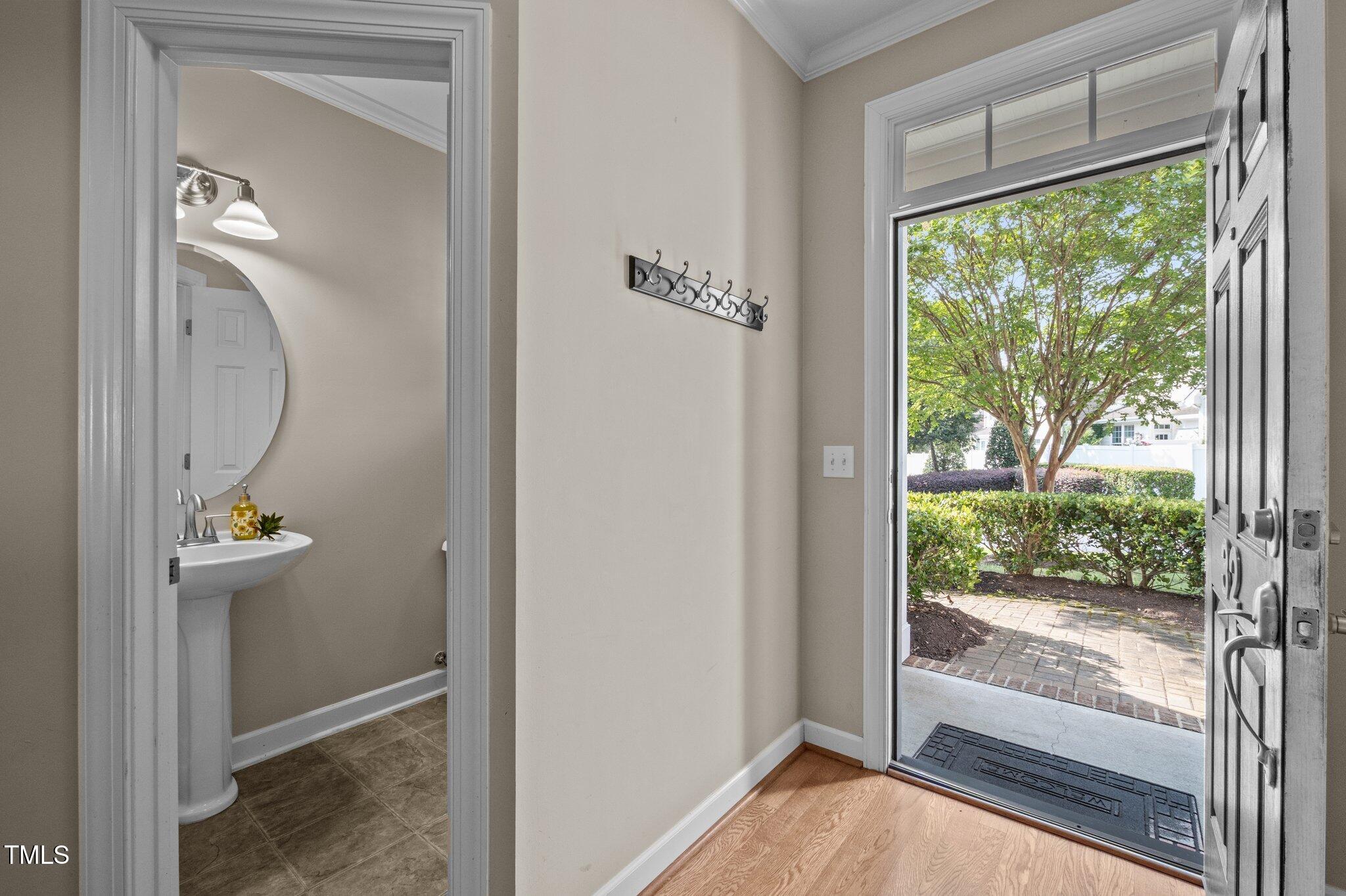 Entryway with an open front door overlooking a leafy tree and a powder room visible through the doorway.