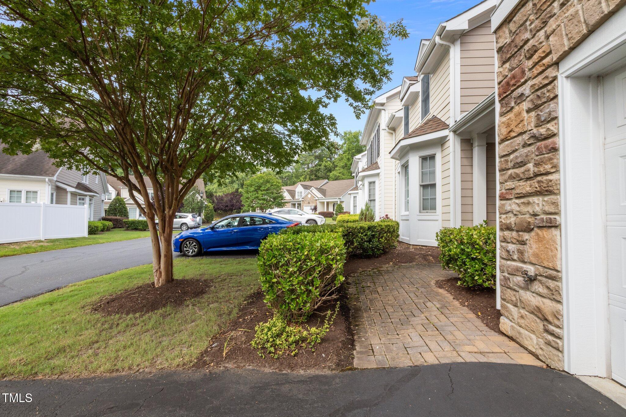 Townhouse entrance with stone façade and brick walkway beside a leafy tree and blue car.
