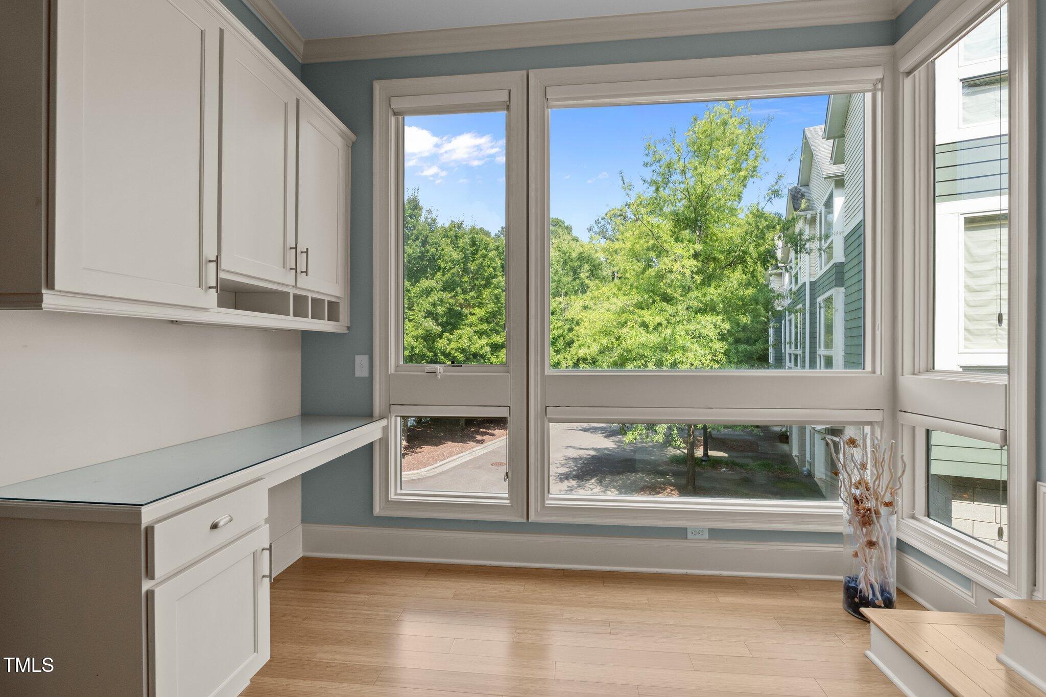Bright room with built-in white cabinetry, light wood floors, and large windows overlooking trees.