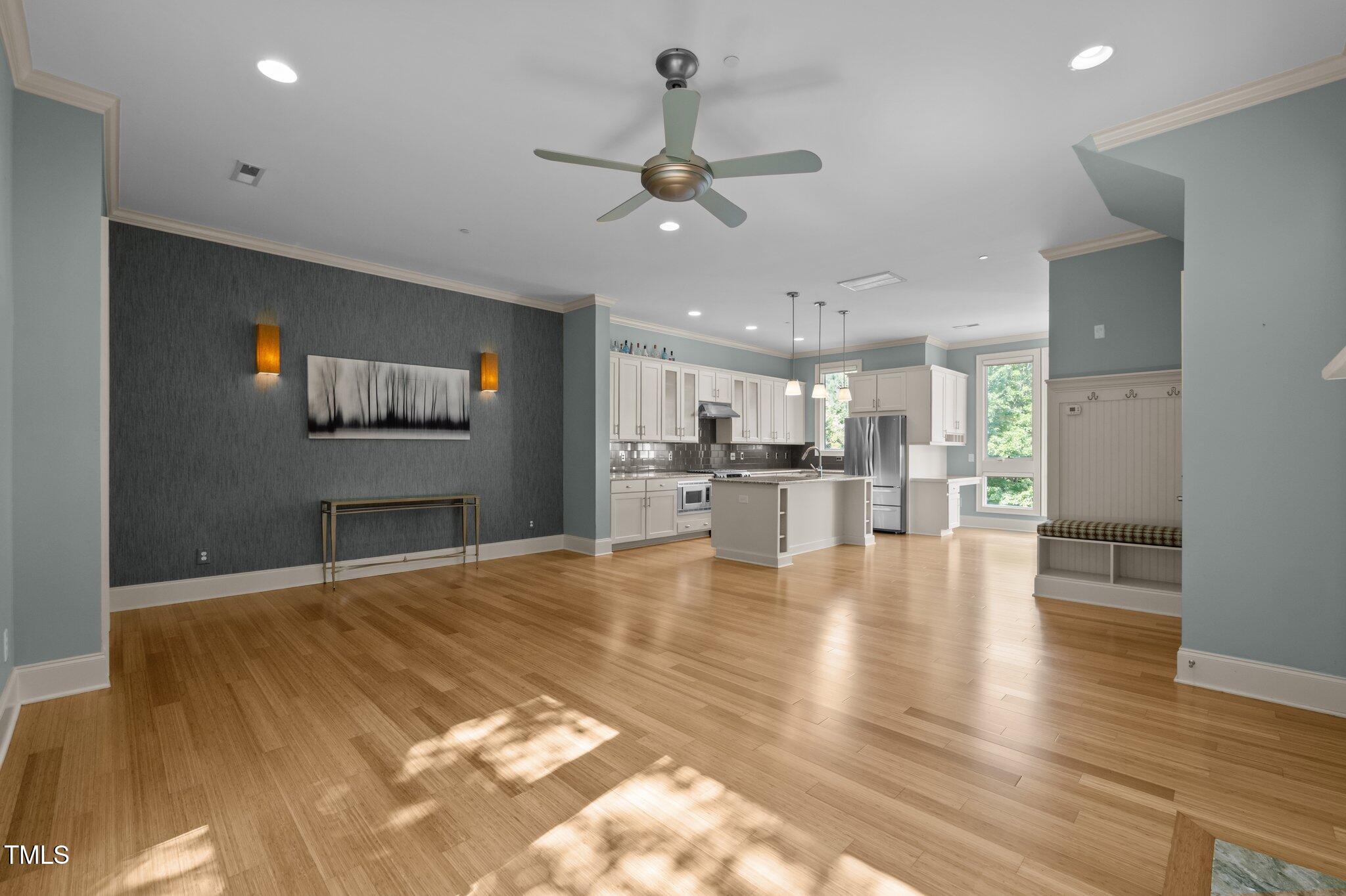 Open-plan living room and kitchen with hardwood floors, white cabinetry, stainless appliances, and a central island.