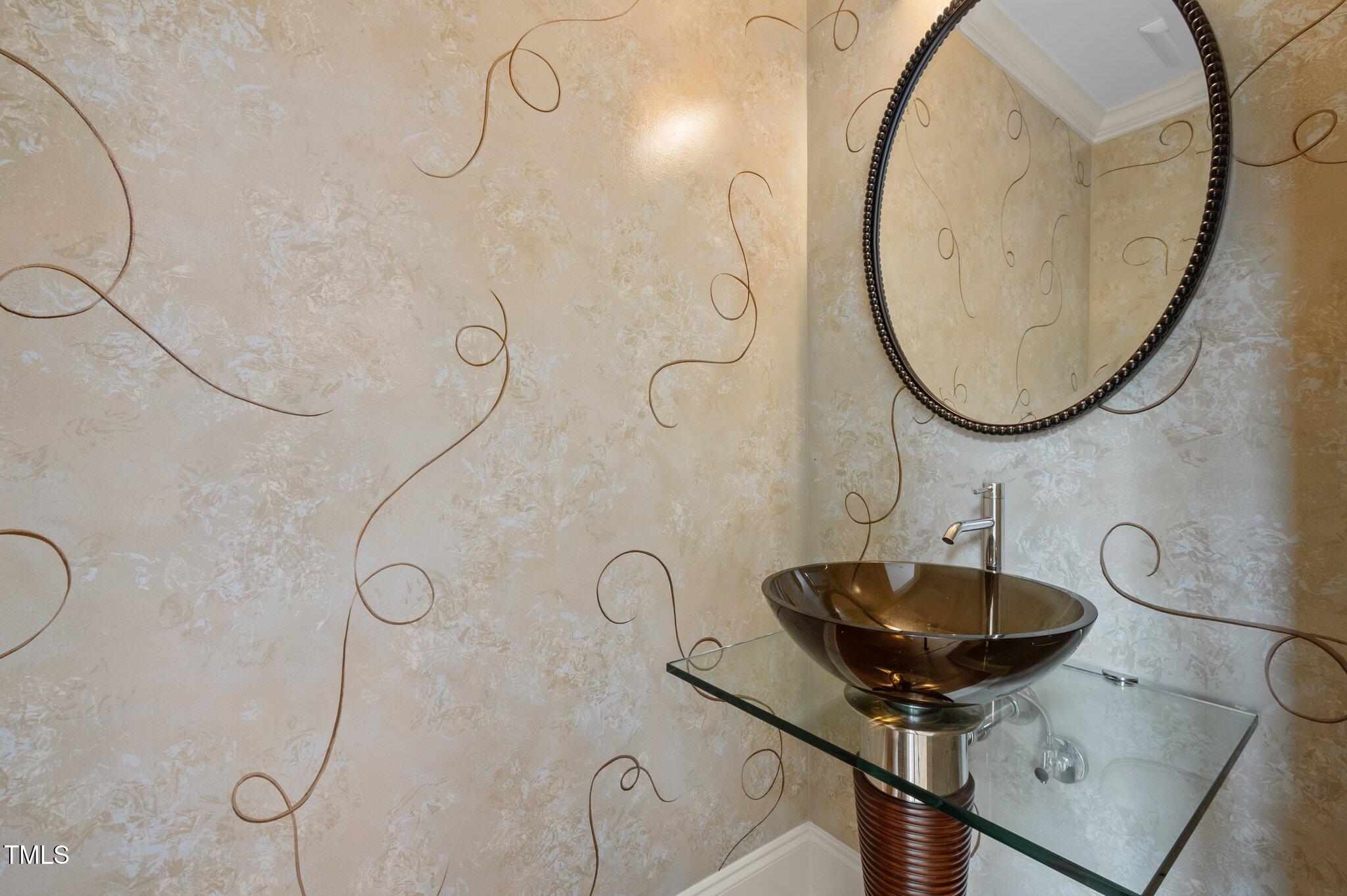 Bathroom vanity with a dark glass vessel sink, glass countertop, and large oval mirror.