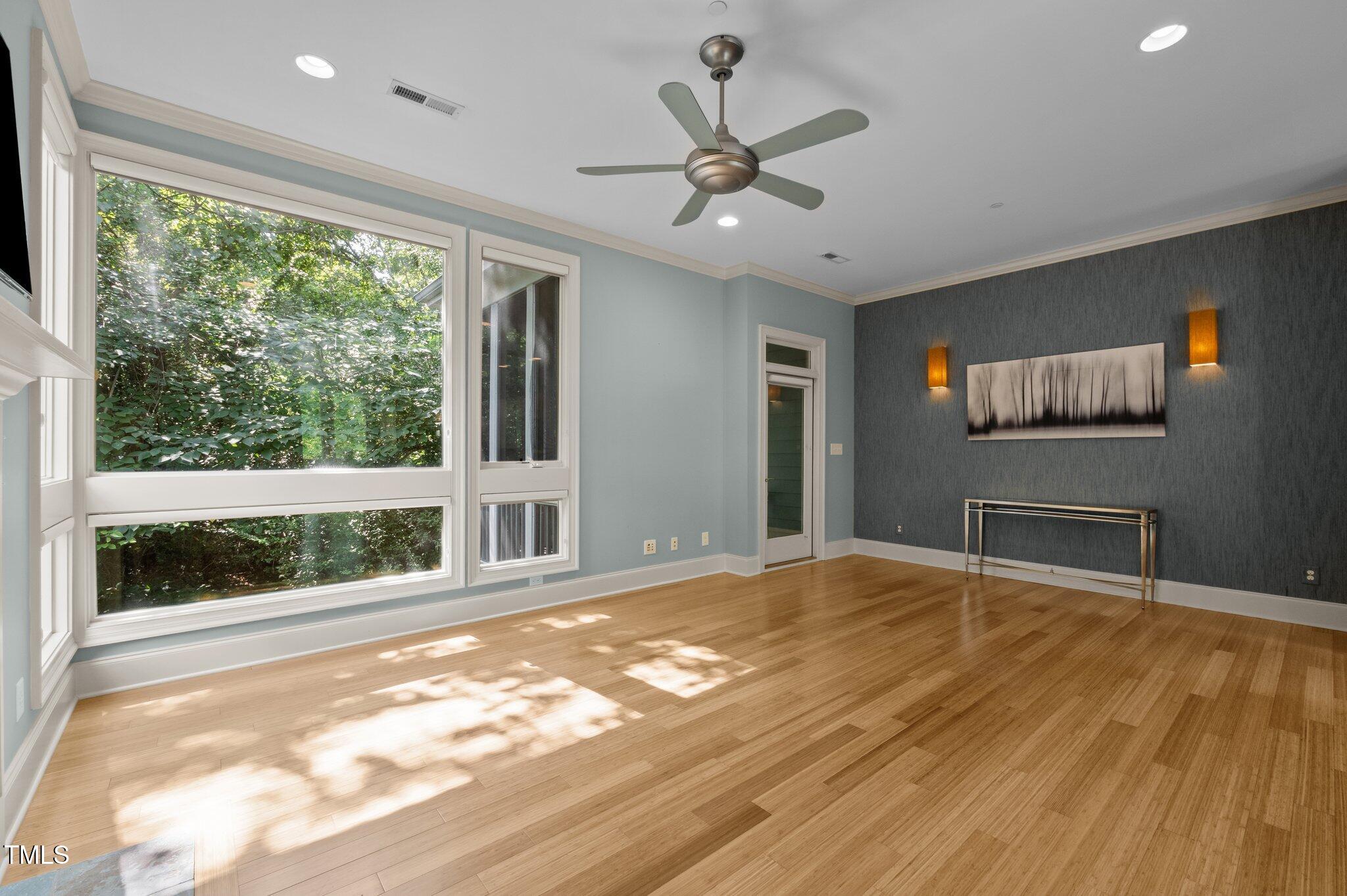 Living room with large tree-facing windows, hardwood floors, and a dark accent wall.