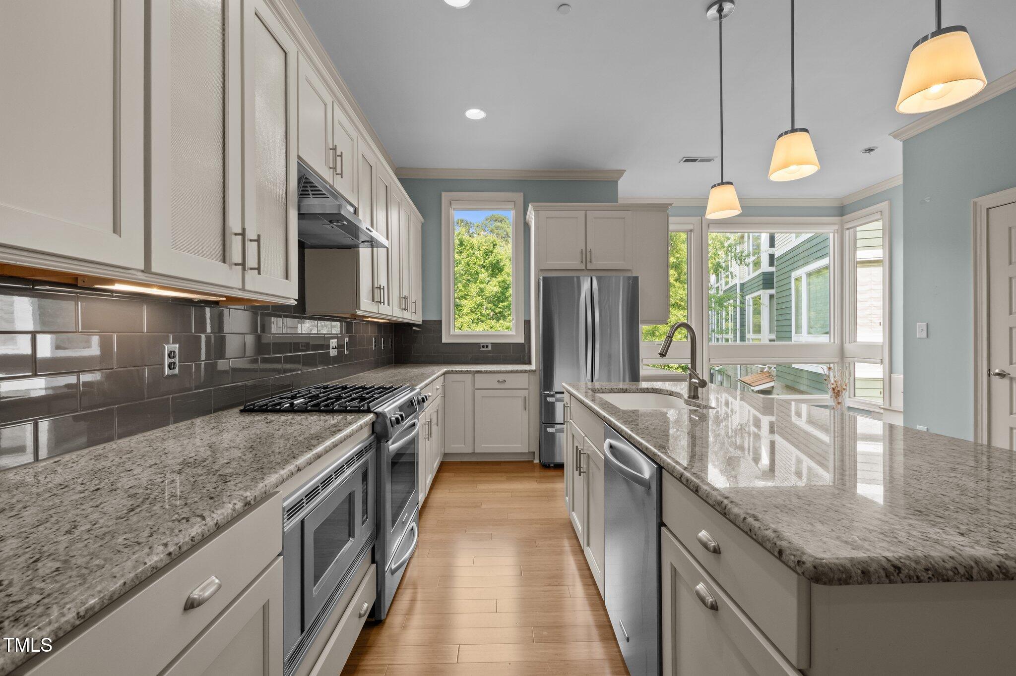 Kitchen with white cabinets, granite counters, stainless steel appliances, and large windows.