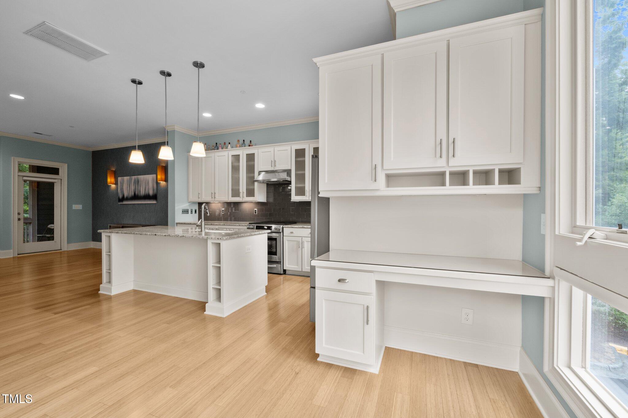 Kitchen with a granite-topped island, white cabinetry, and a built-in desk beside large windows.