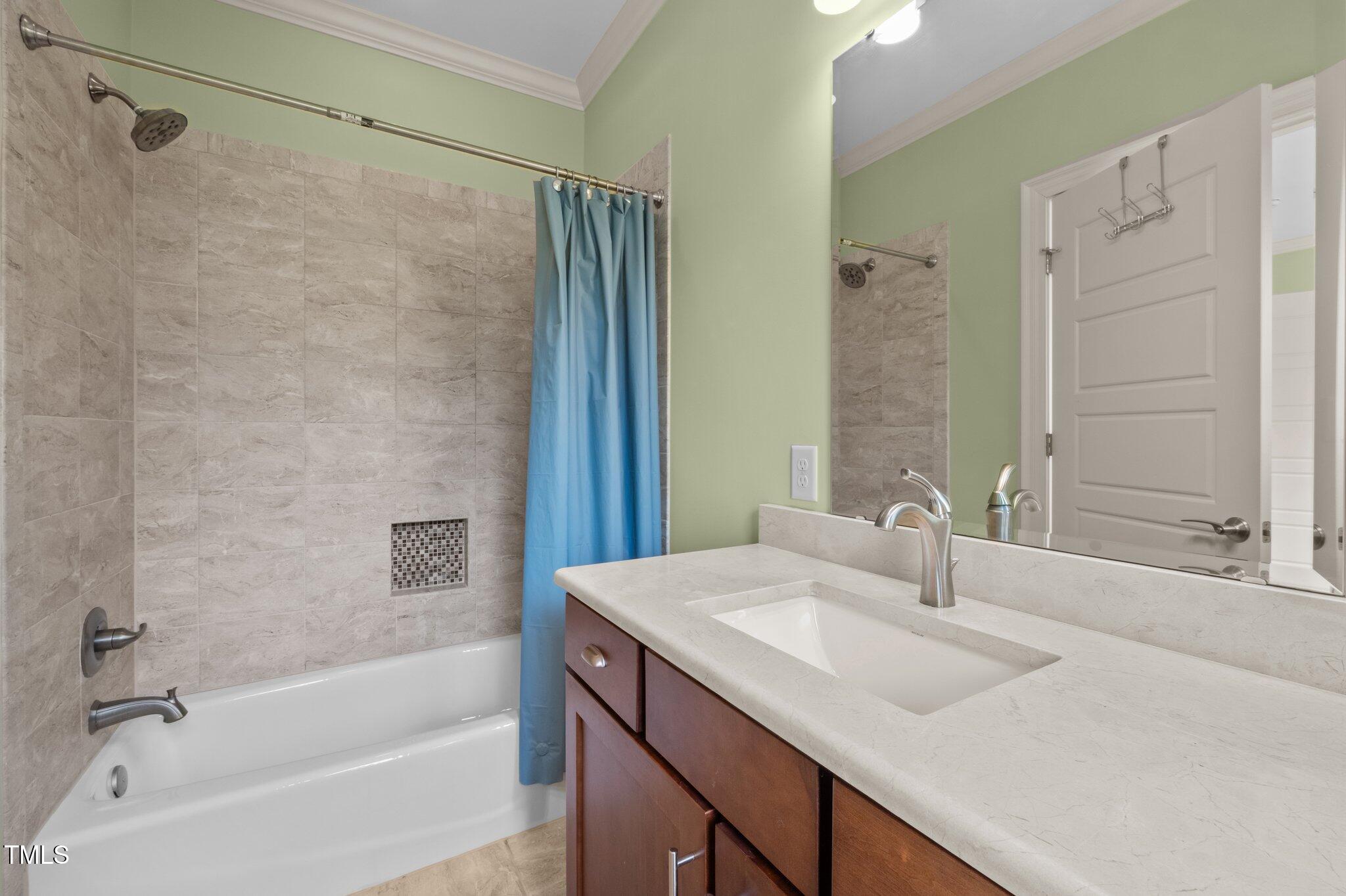 Bathroom with a tiled tub and blue shower curtain beside a dark wood vanity.