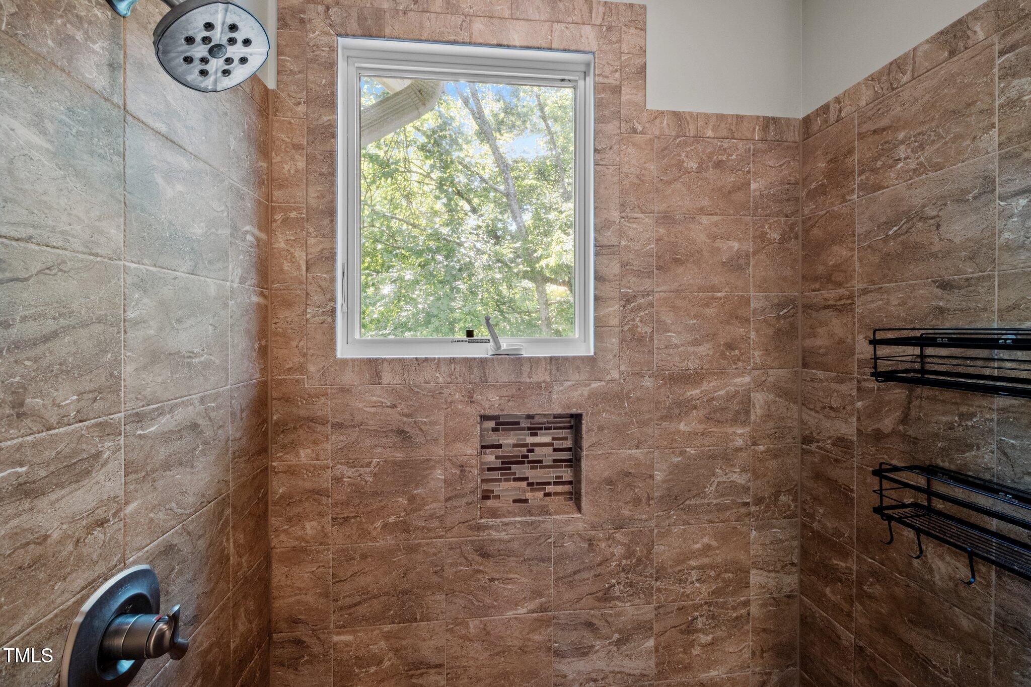 Walk-in shower with brown tile, a window overlooking trees, and a built-in mosaic niche.
