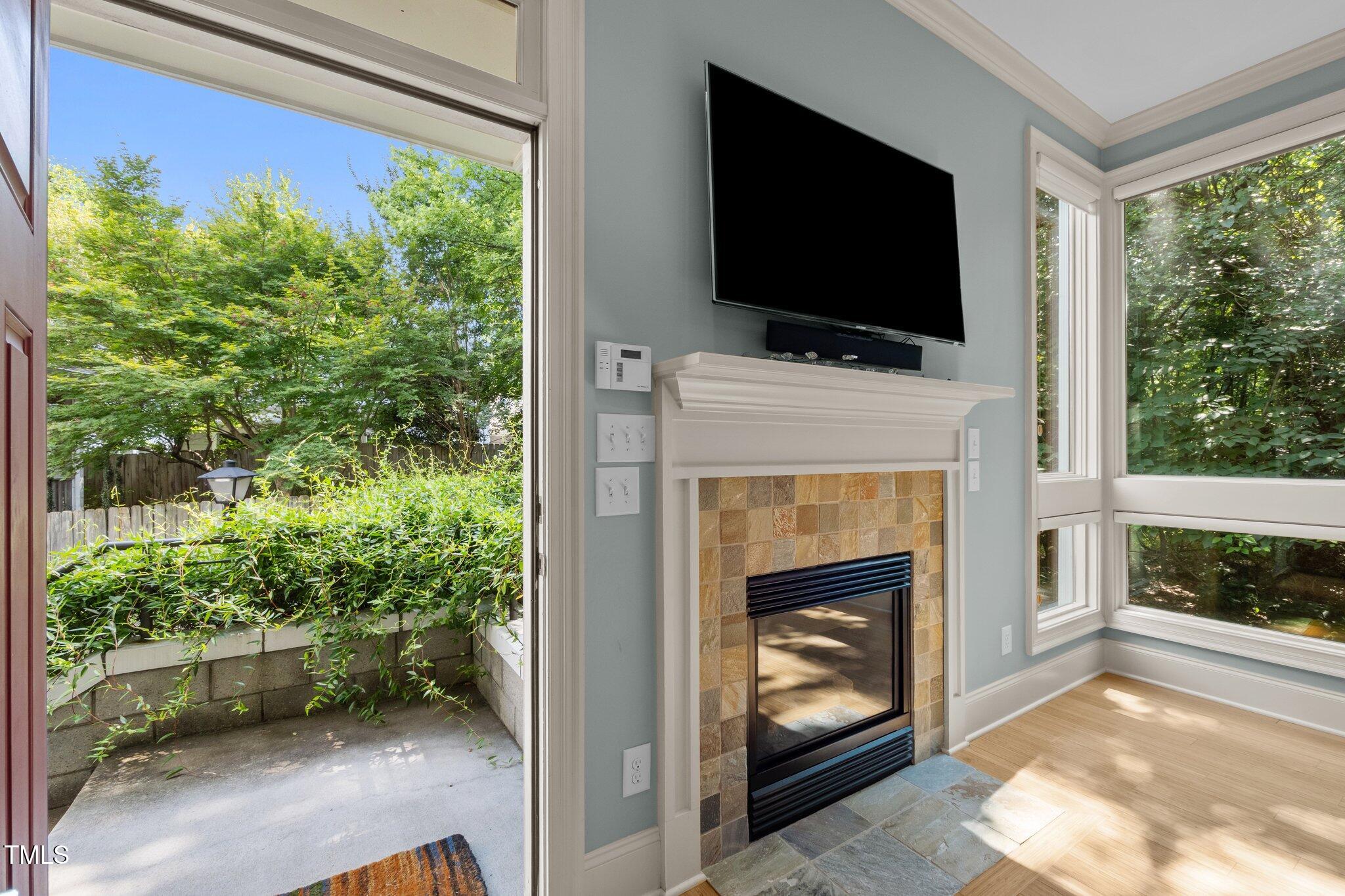 Living room with tiled fireplace and mounted TV, opening onto a leafy private patio.