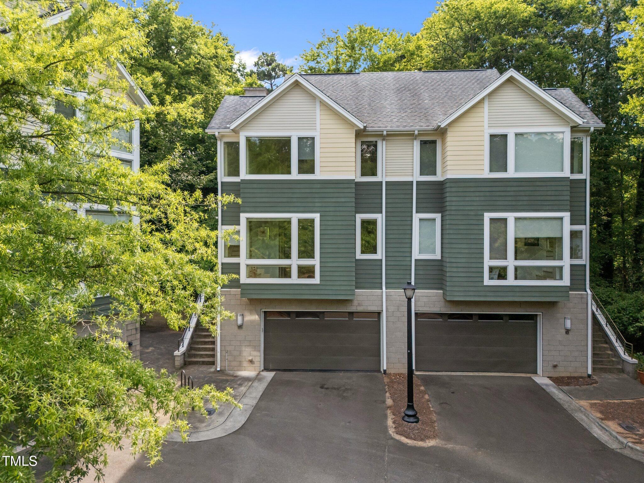 Two-story townhouse with cream and green siding, two garages, and leafy trees.