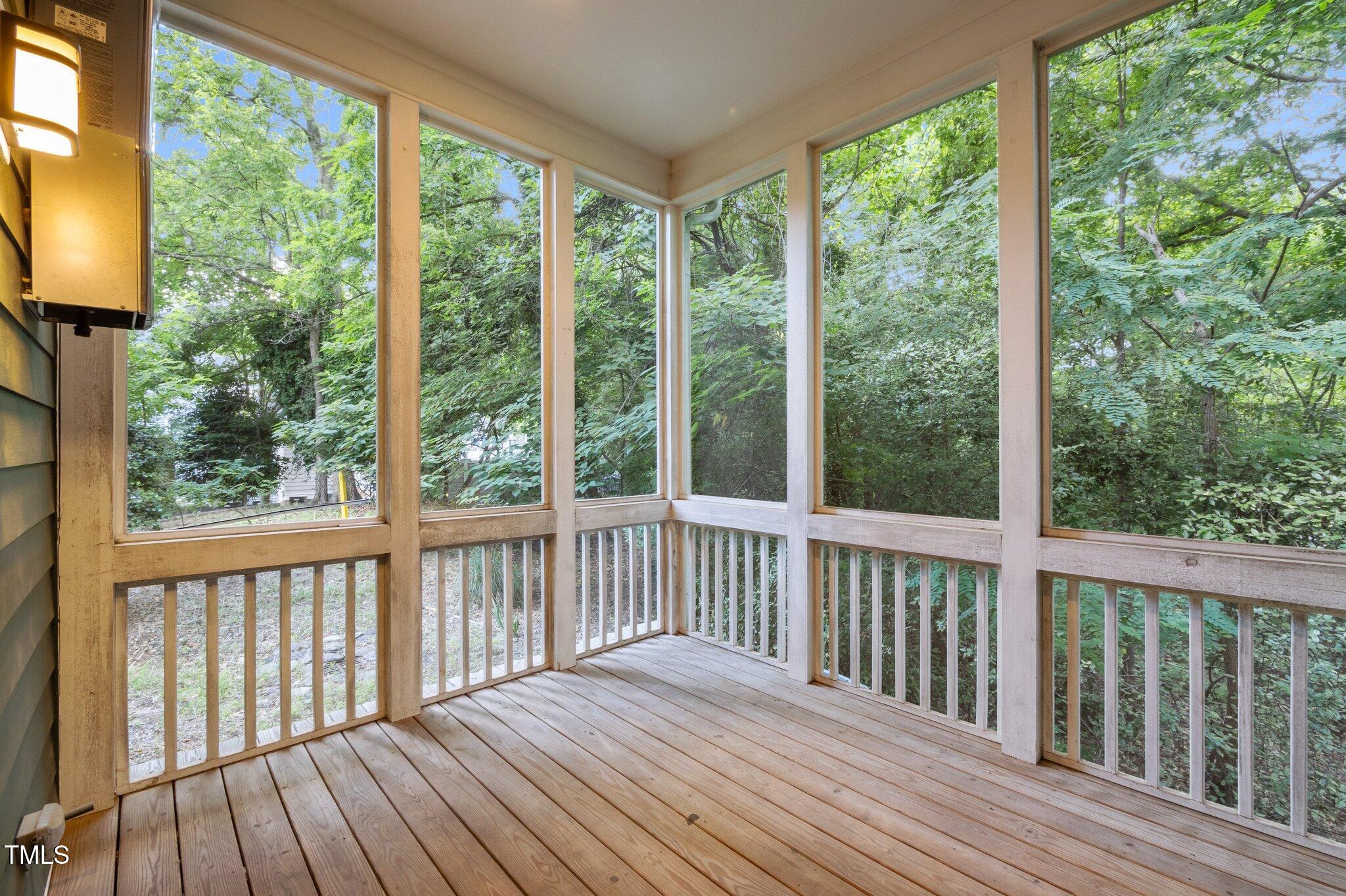 Screened porch with a wood-plank floor and large windows overlooking trees.