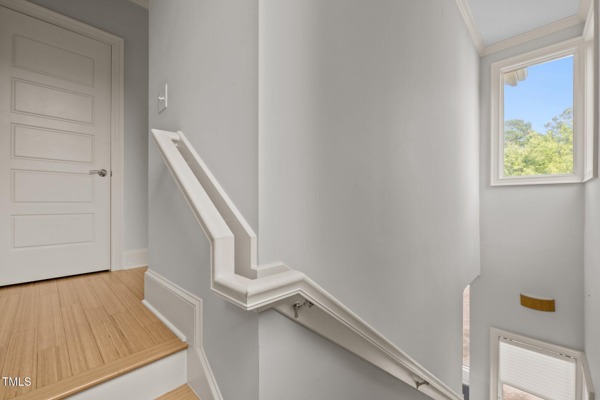 Bright stairwell with white handrails, a wood-floored landing, and a window overlooking trees.