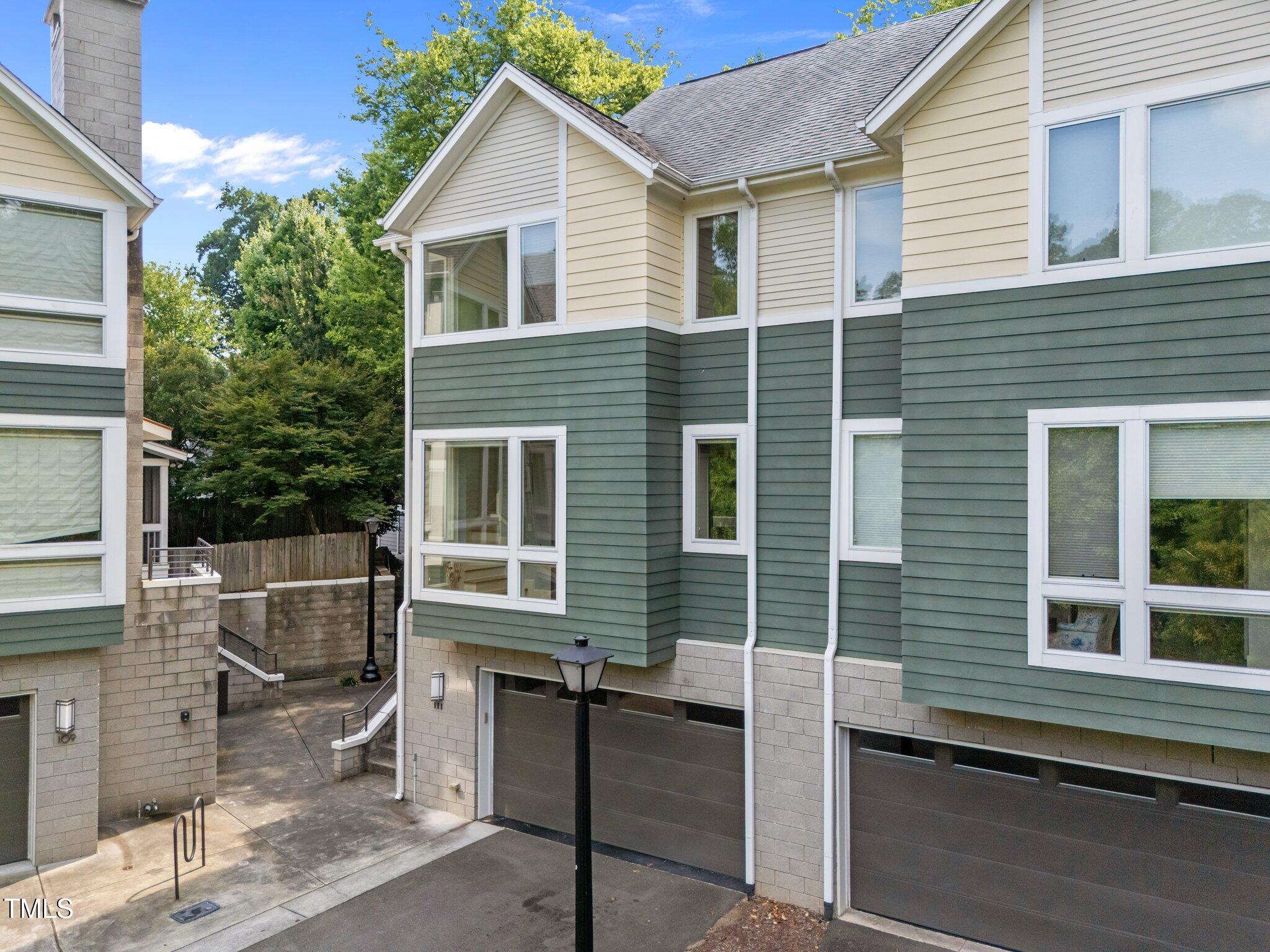 Residential building with cream and green siding, attached garages, and a paved courtyard.