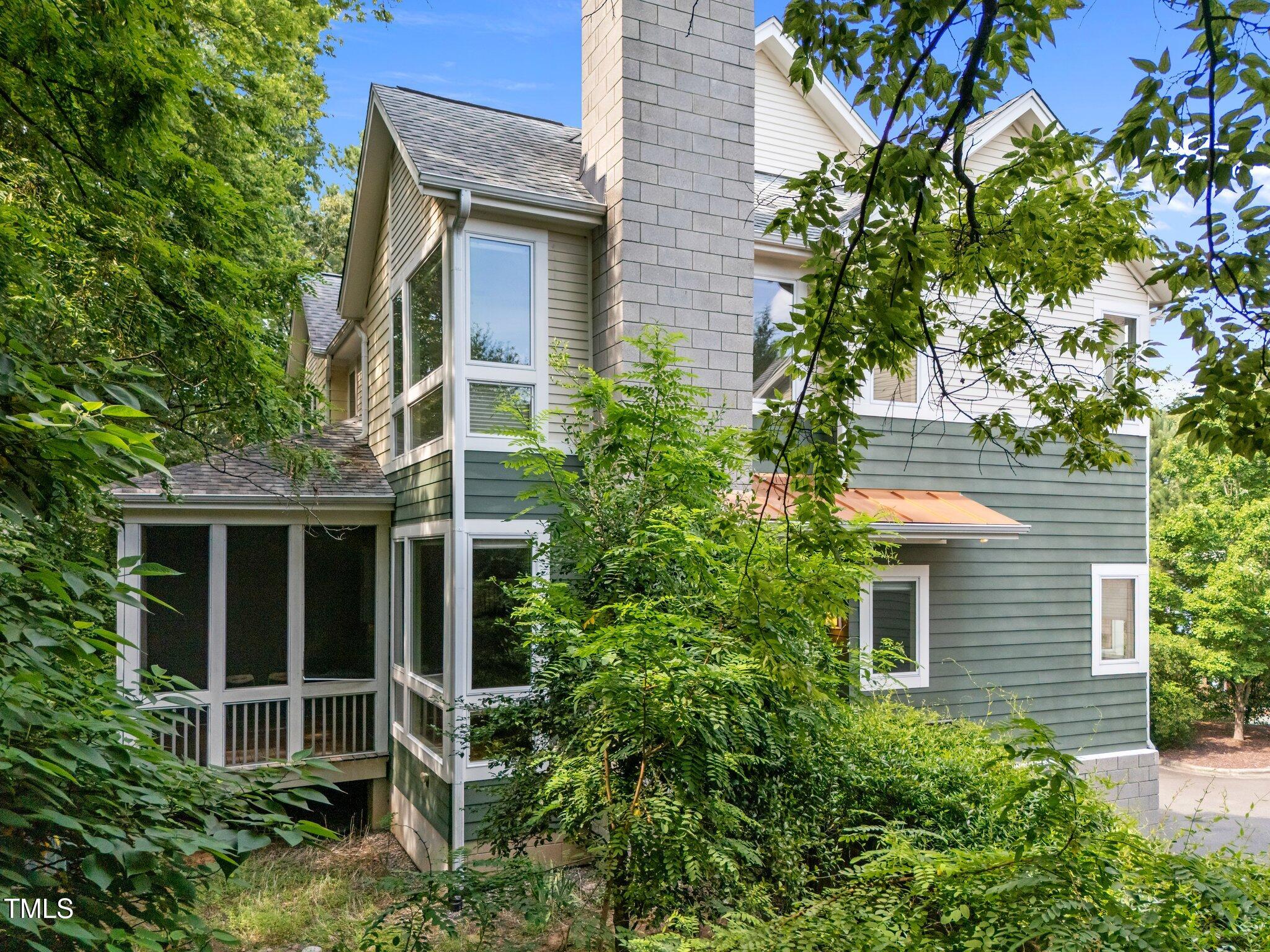 Home exterior with a screened porch, tall masonry chimney, and mature surrounding trees.