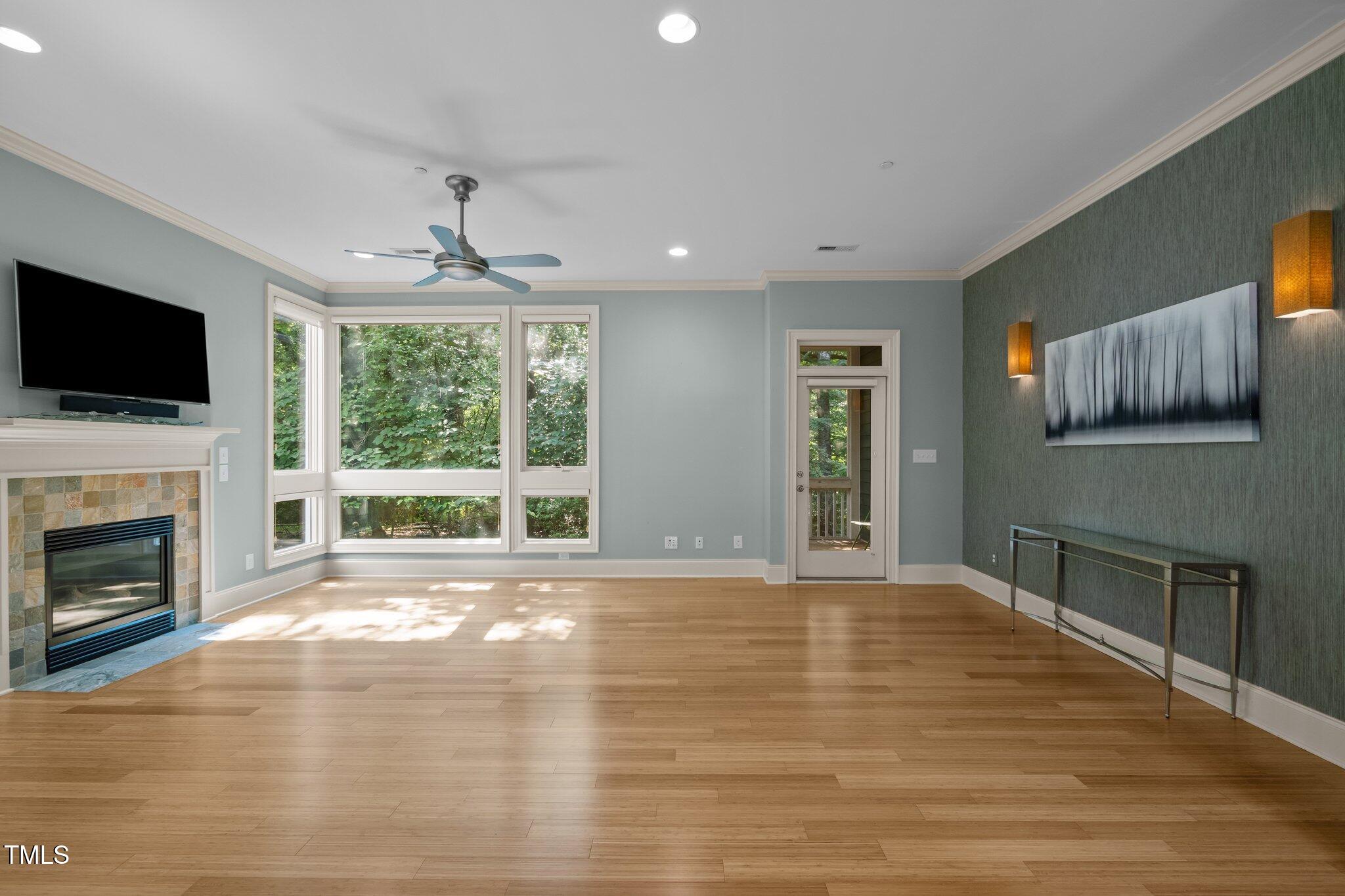 Living room with hardwood floors, tiled fireplace, and large windows overlooking trees.