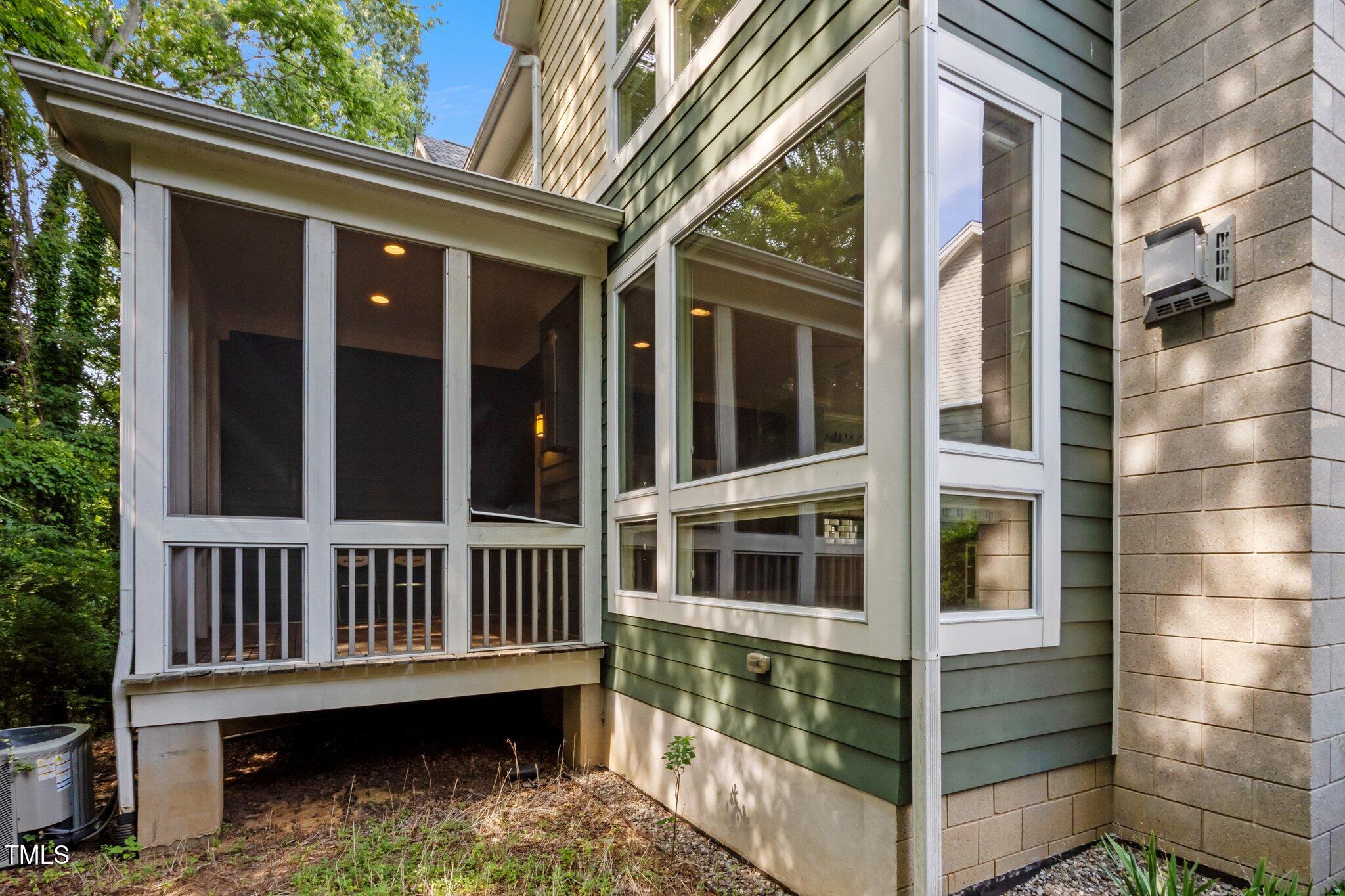 Home exterior with a large screened porch and tall windows beside a block wall.