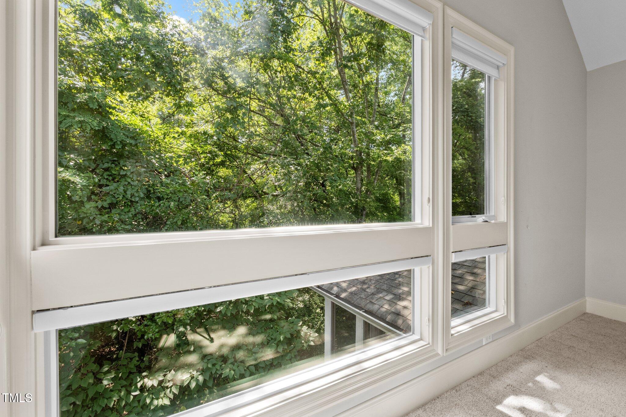 Empty room with large windows overlooking dense green trees.