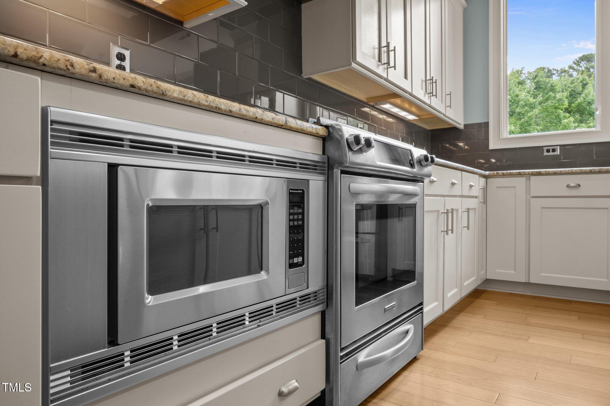 Kitchen with stainless steel built-in microwave and oven, white cabinets, and dark tile backsplash.
