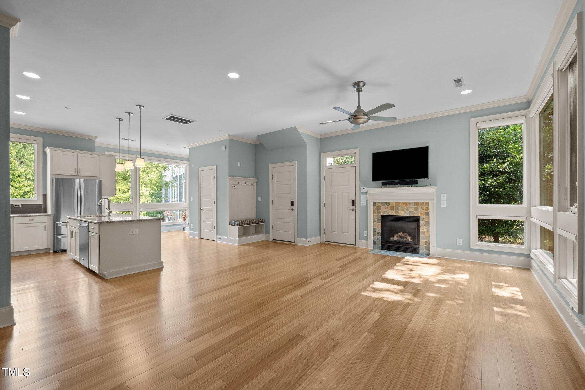 Open-plan living room and kitchen with a fireplace, island, light wood floors, and large windows.
