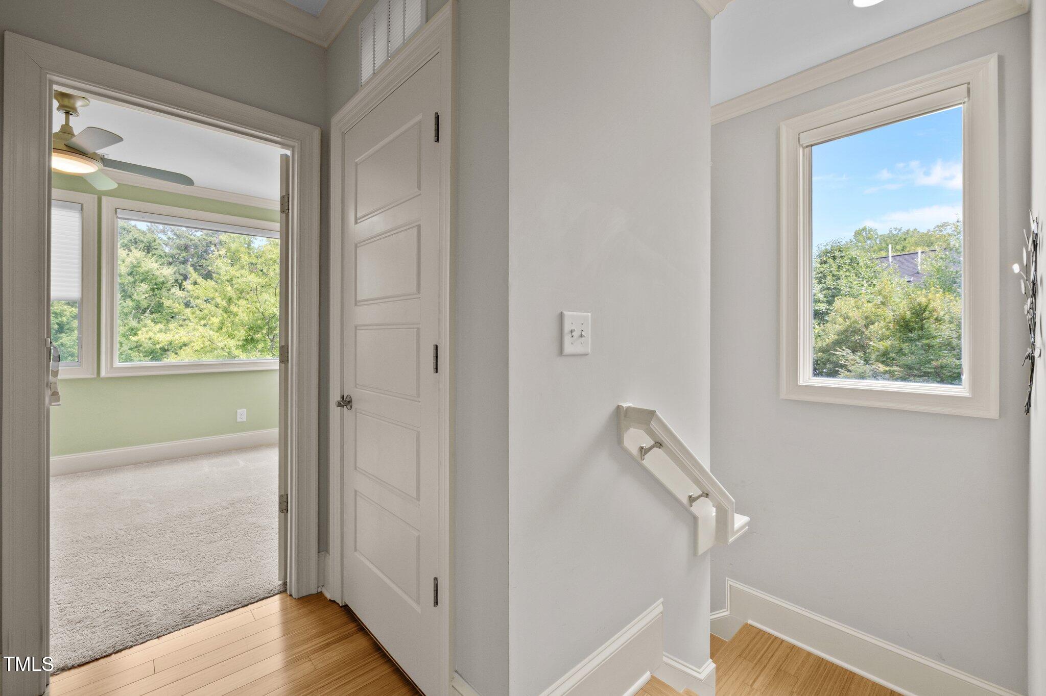 Stair landing with hardwood floors and a large window, beside an open doorway to a carpeted room.