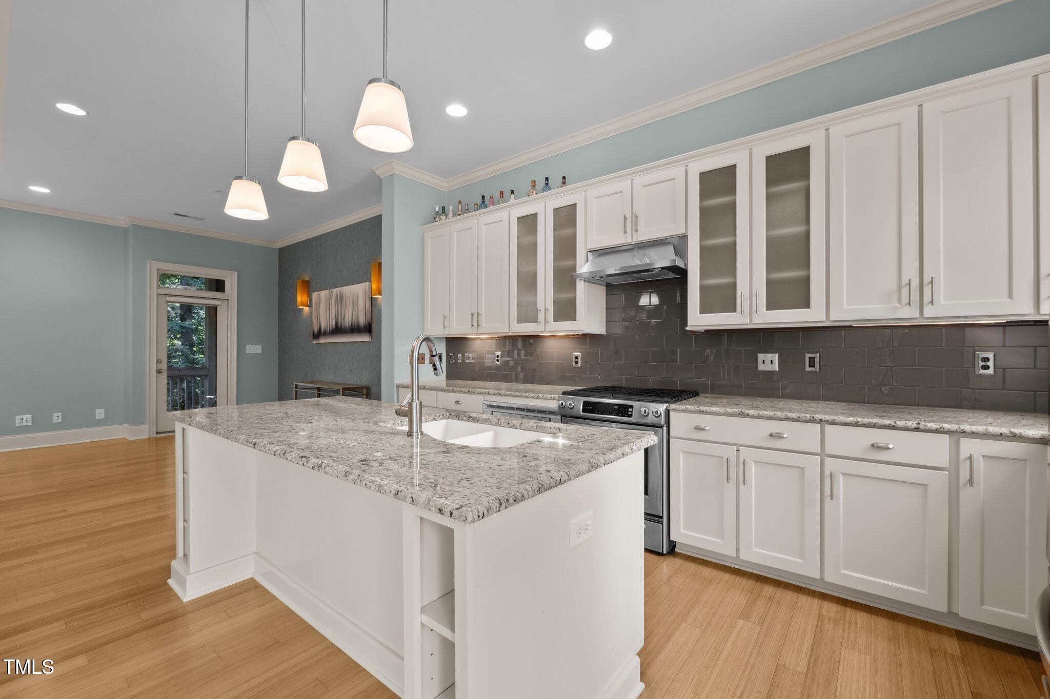 Modern kitchen with a granite island, white cabinets, stainless steel range, and dark tile backsplash.