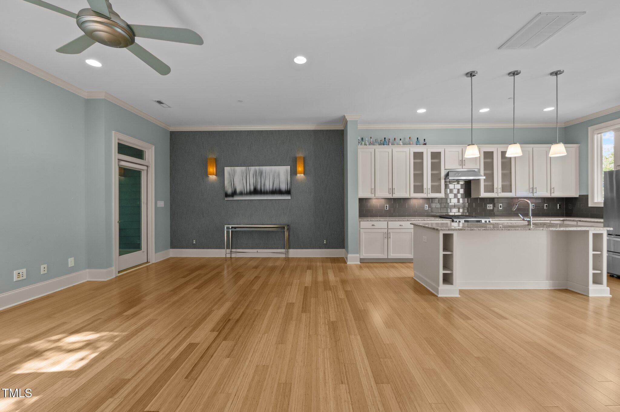 Open kitchen and living area with a large white island, pendant lights, and sunlit wood floors.