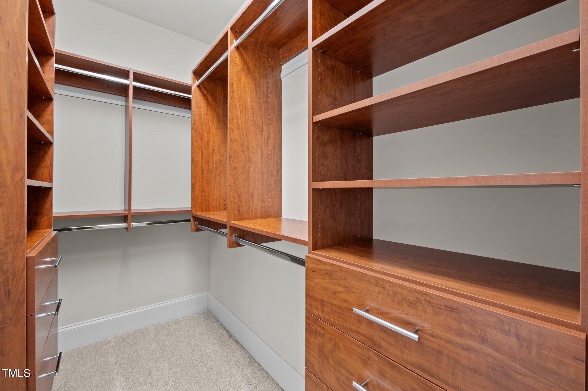 Walk-in closet with reddish-brown built-in shelving, hanging rails, and drawers.