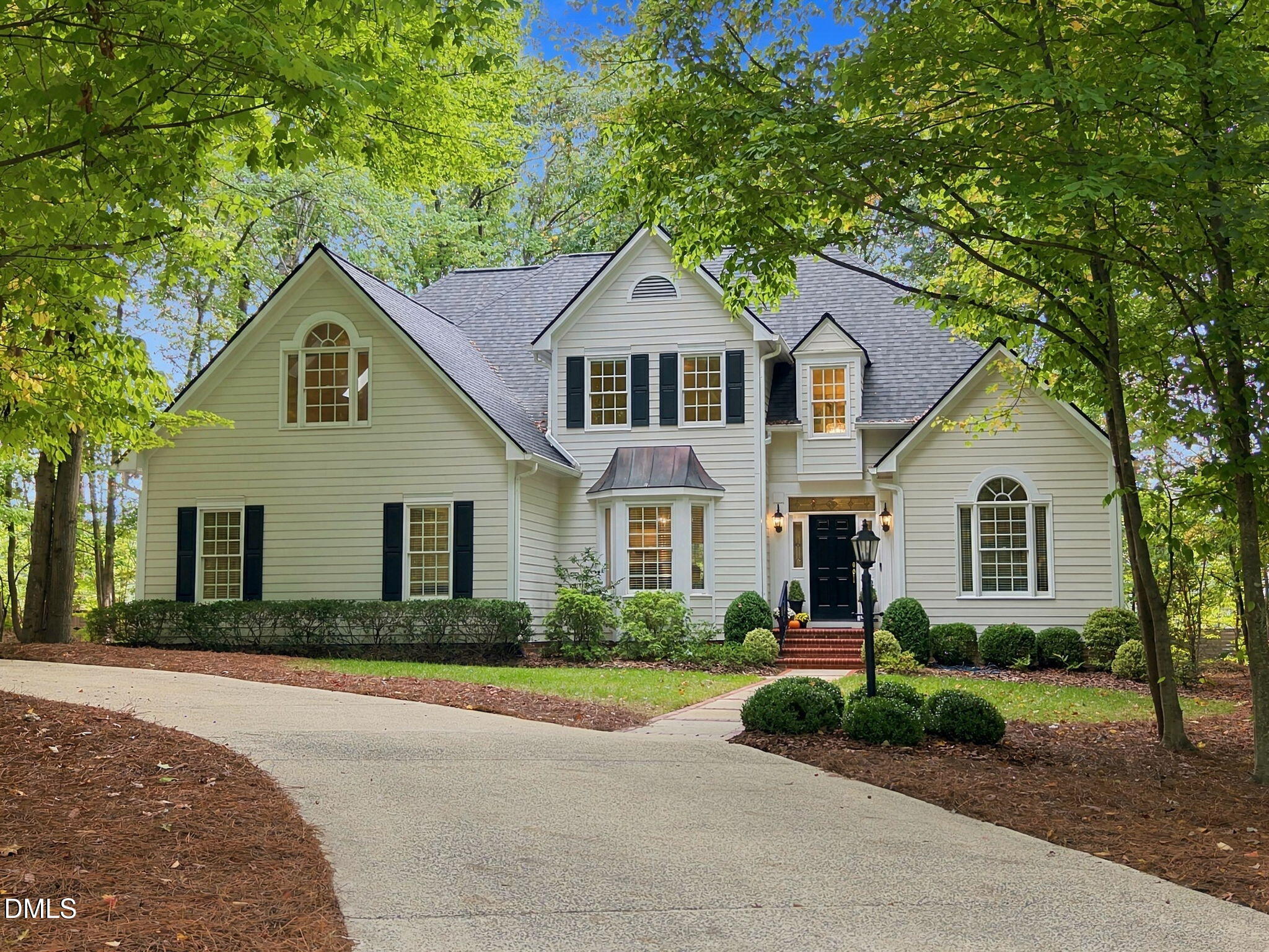 Two-story home with dark shutters and multiple gables, framed by leafy trees beside a curved driveway.
