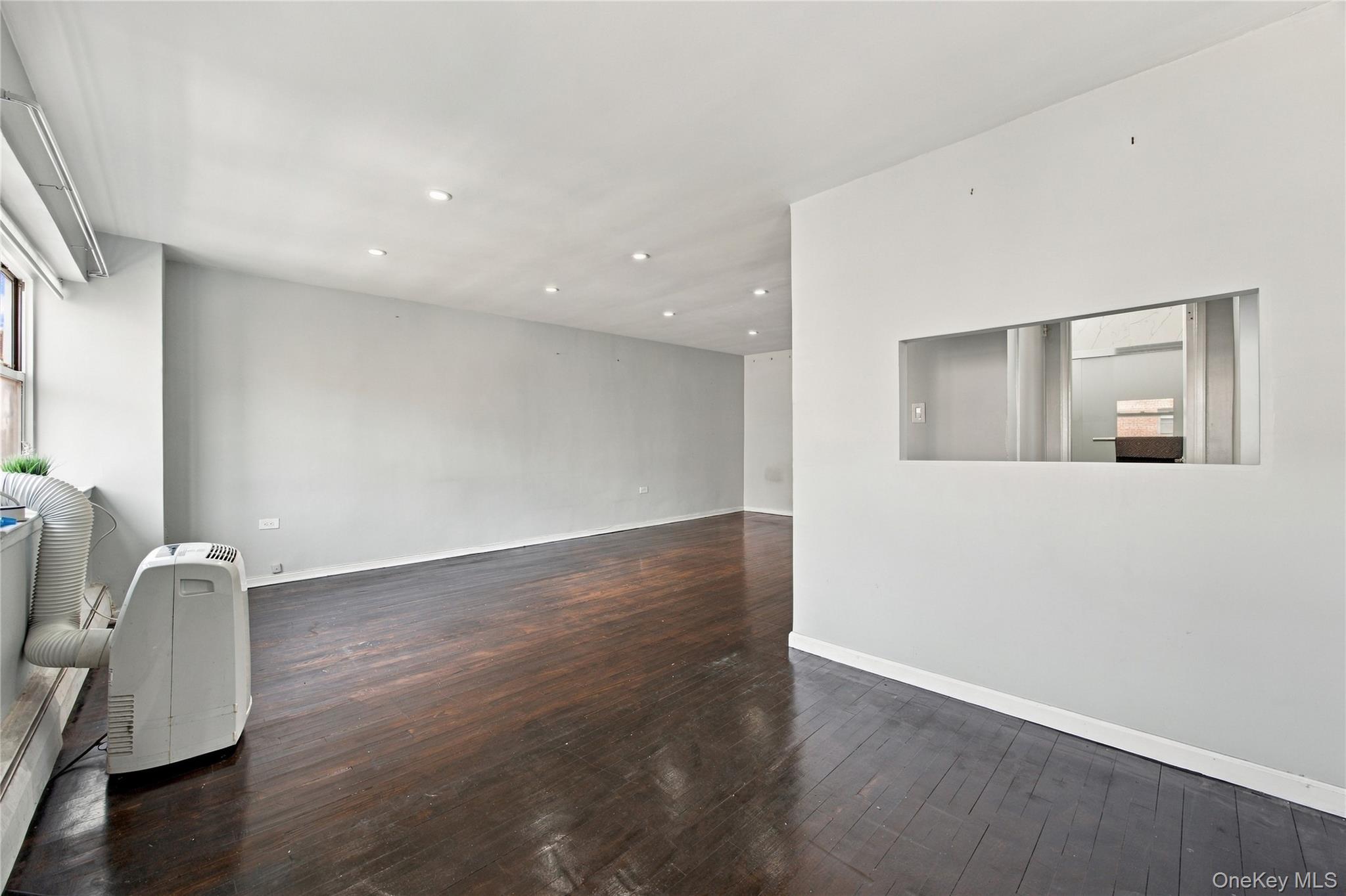 Vacant room with dark hardwood floors, recessed lights, and a wide interior pass-through opening.