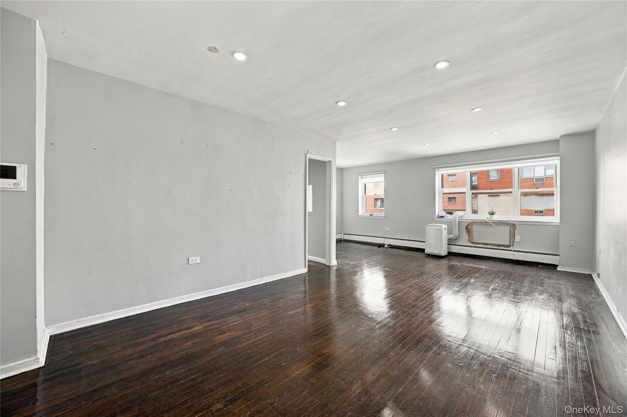 Empty gray living room with dark hardwood floors, wide windows, and a portable air conditioner.