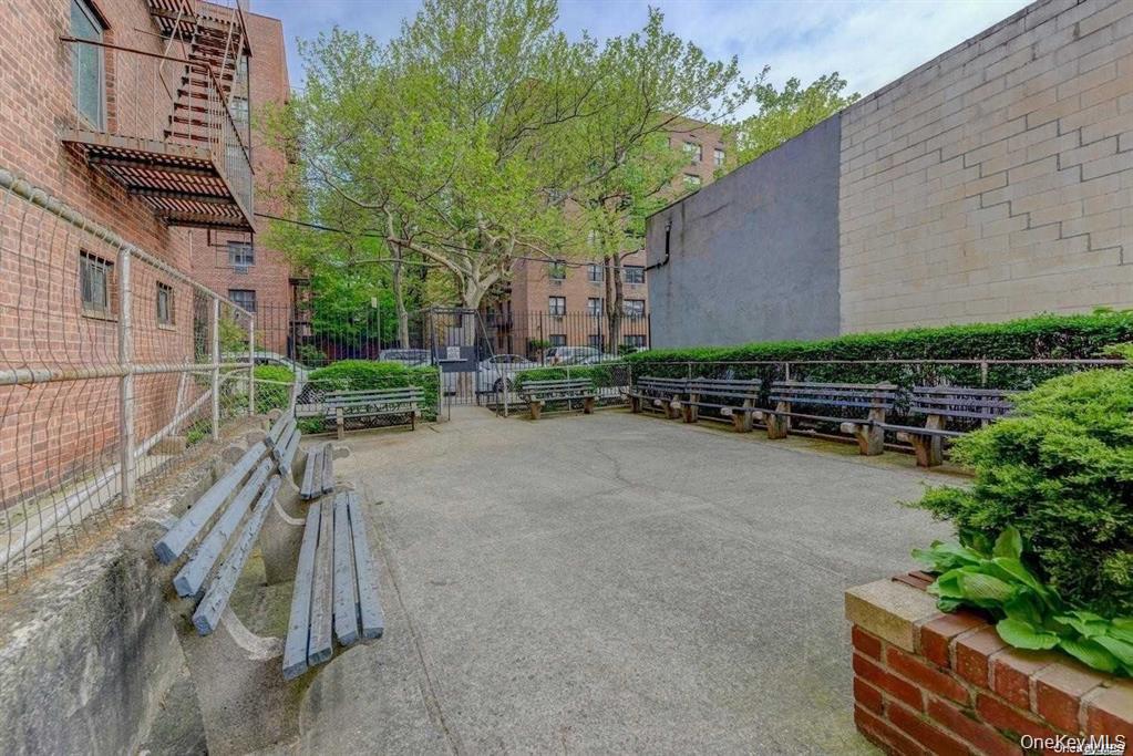 Residential courtyard with rows of benches, mature trees, and a paved seating area.