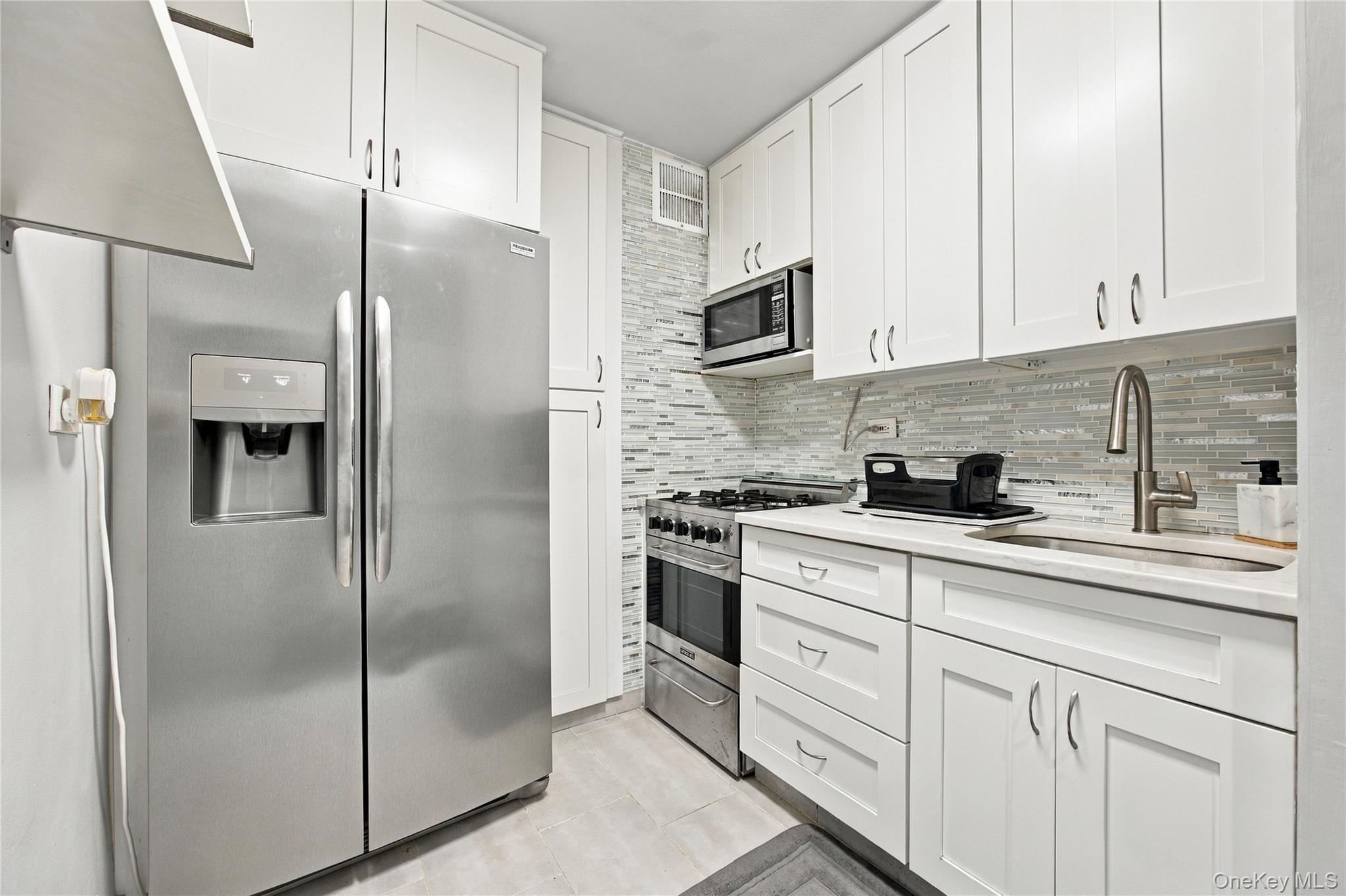 Kitchen with white cabinets, stainless steel appliances, and a gray mosaic tile backsplash.