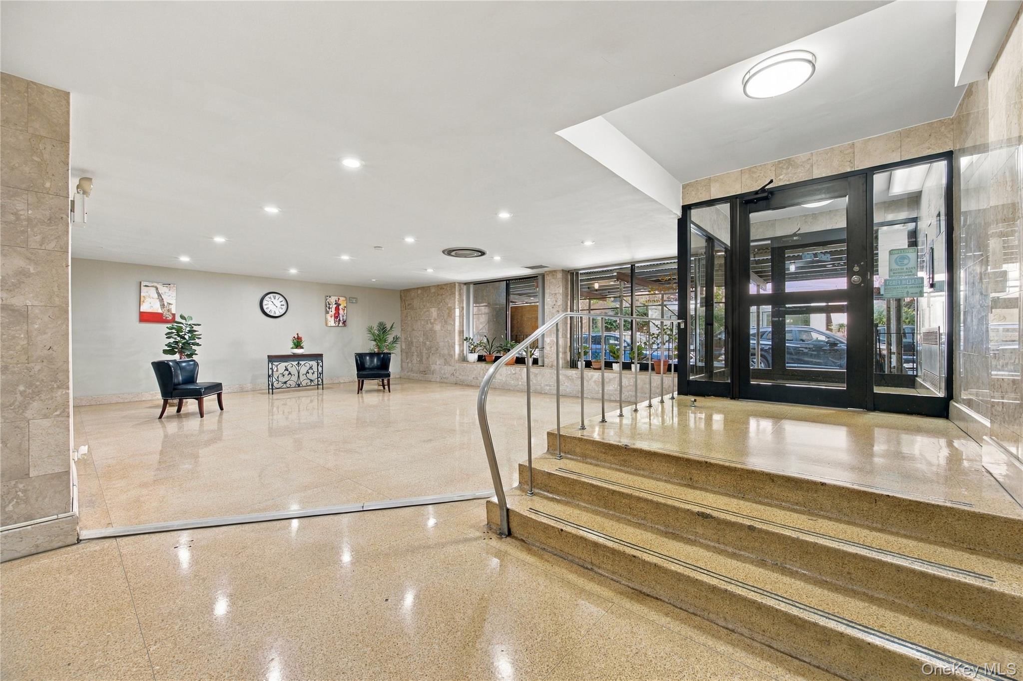 Apartment building lobby with a glass entrance, polished stone floors, steps, and a small seating area.