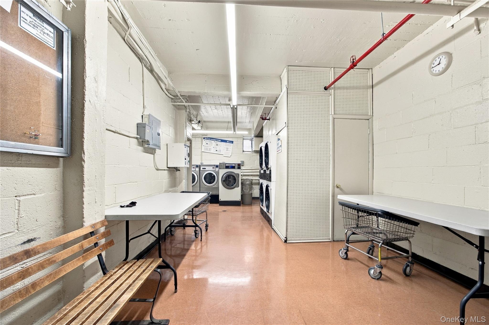 Shared laundry room with front-loading machines, folding tables, and rolling laundry carts.