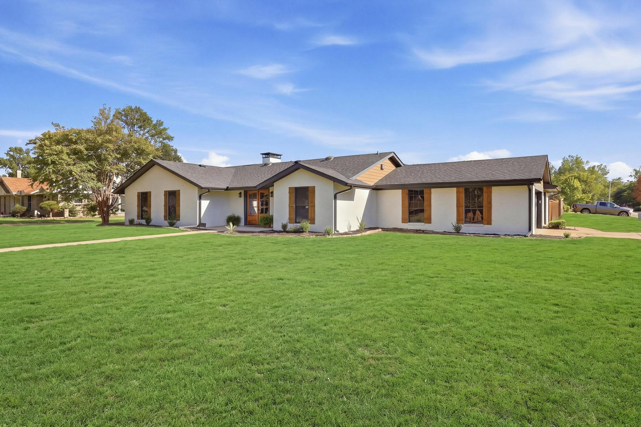 Single-story white home with wood shutters and a broad green lawn.