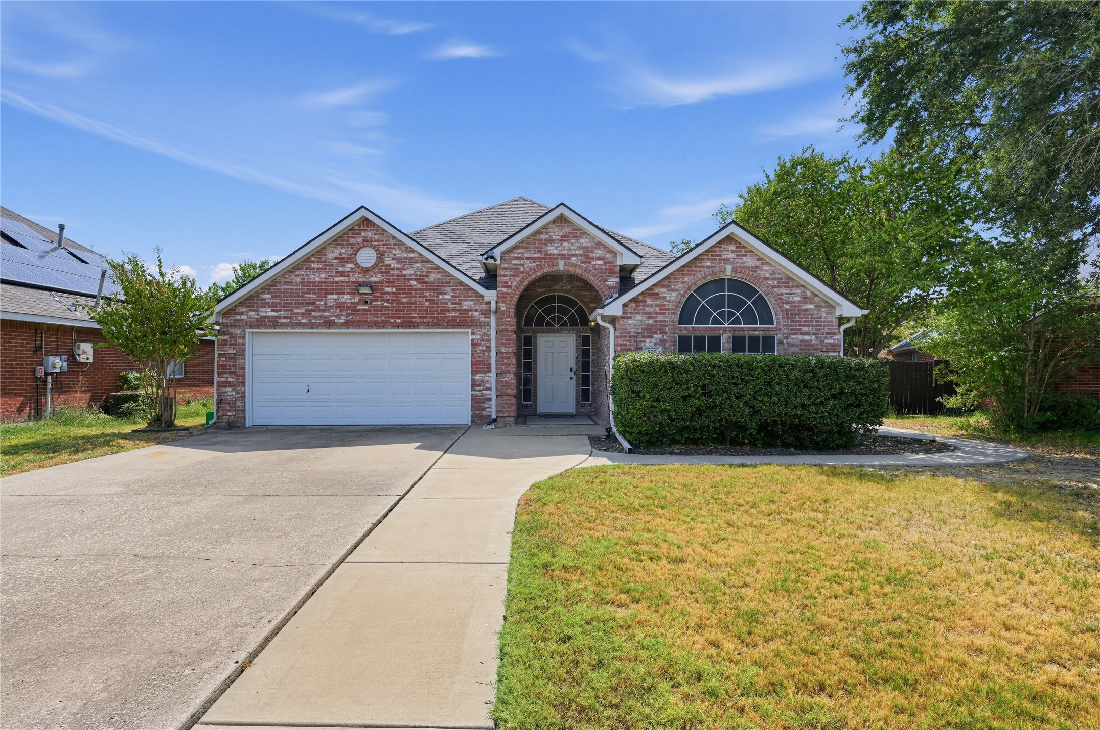 Red brick house with a white double garage door, arched windows, and a wide concrete driveway.