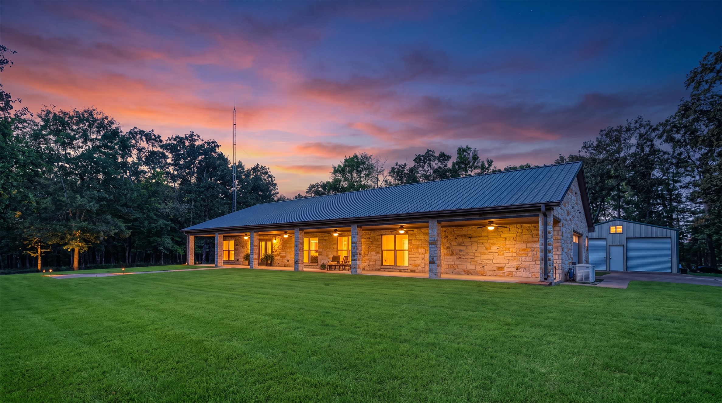 Stone house with a metal roof and illuminated covered porch at dusk.