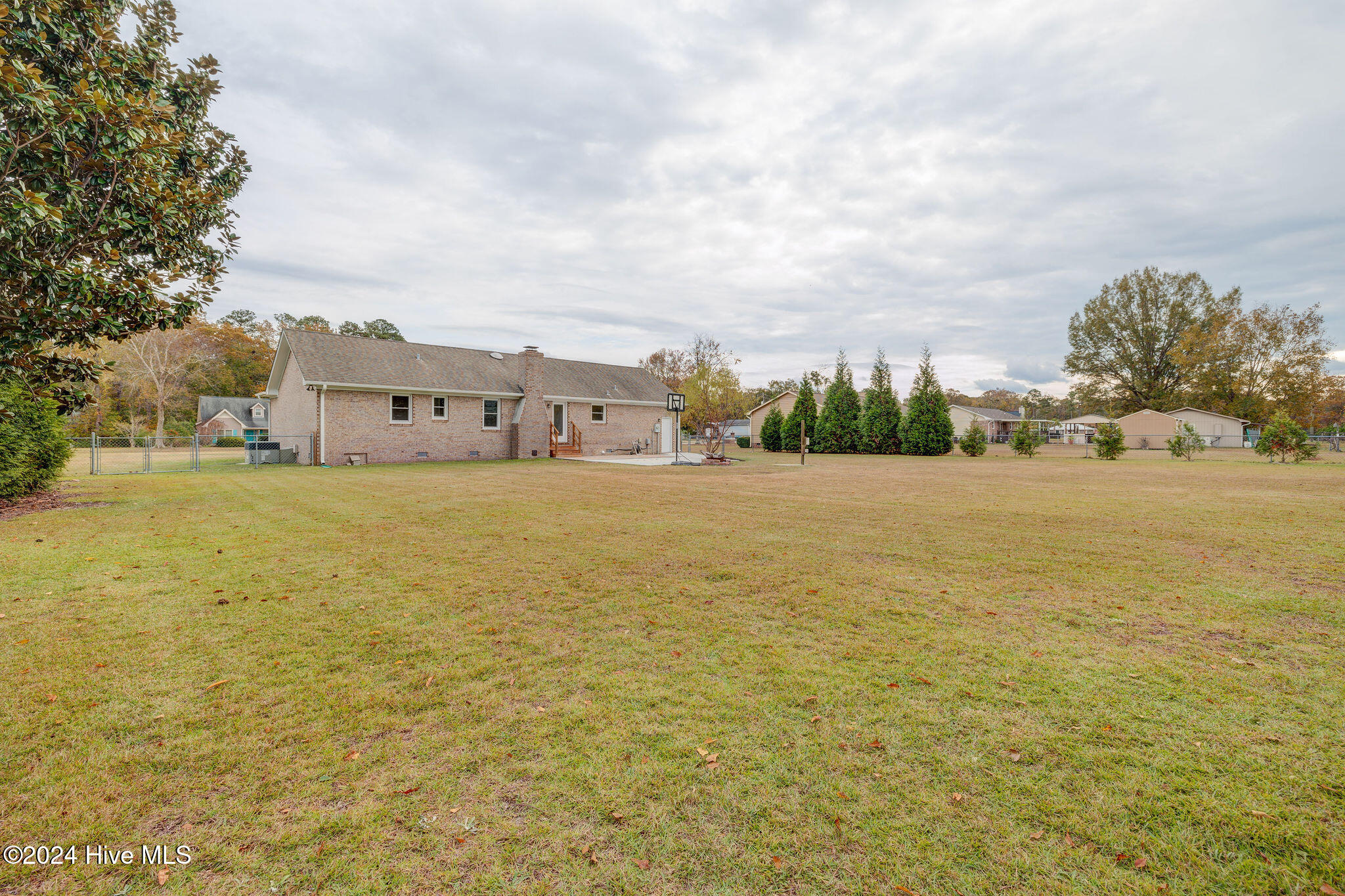 Brick home behind a broad lawn, with a basketball hoop and autumn trees.