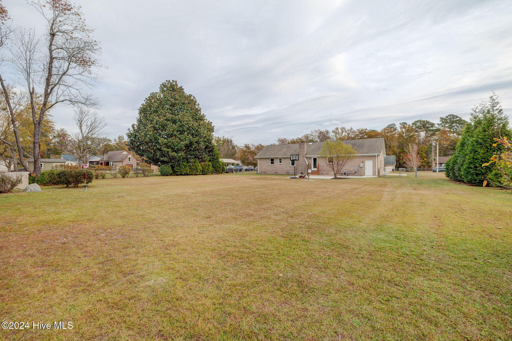Brick home viewed across a spacious backyard, with a basketball hoop near the house.