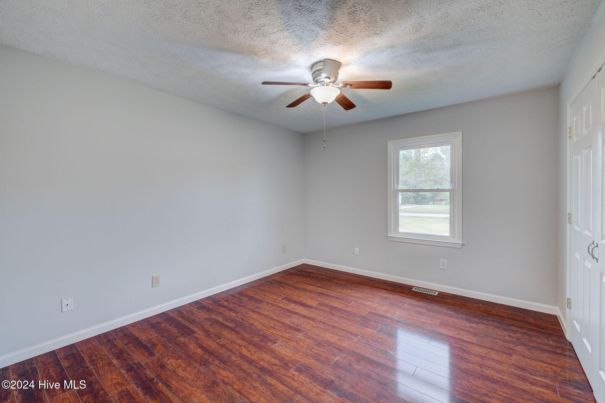 Empty bedroom with reddish-brown wood-look floors, a ceiling fan, and white closet doors.