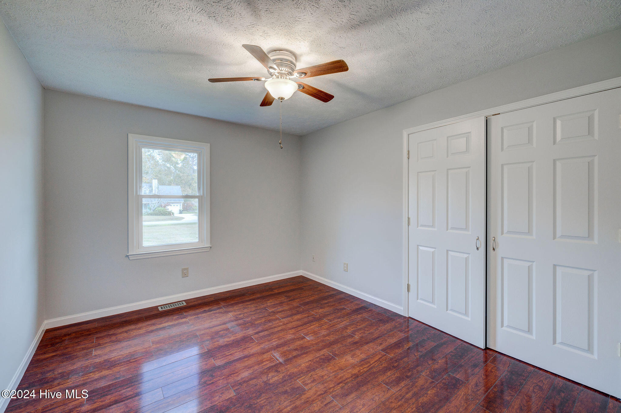 Empty bedroom with dark wood-look flooring, white closet doors, and a ceiling fan.