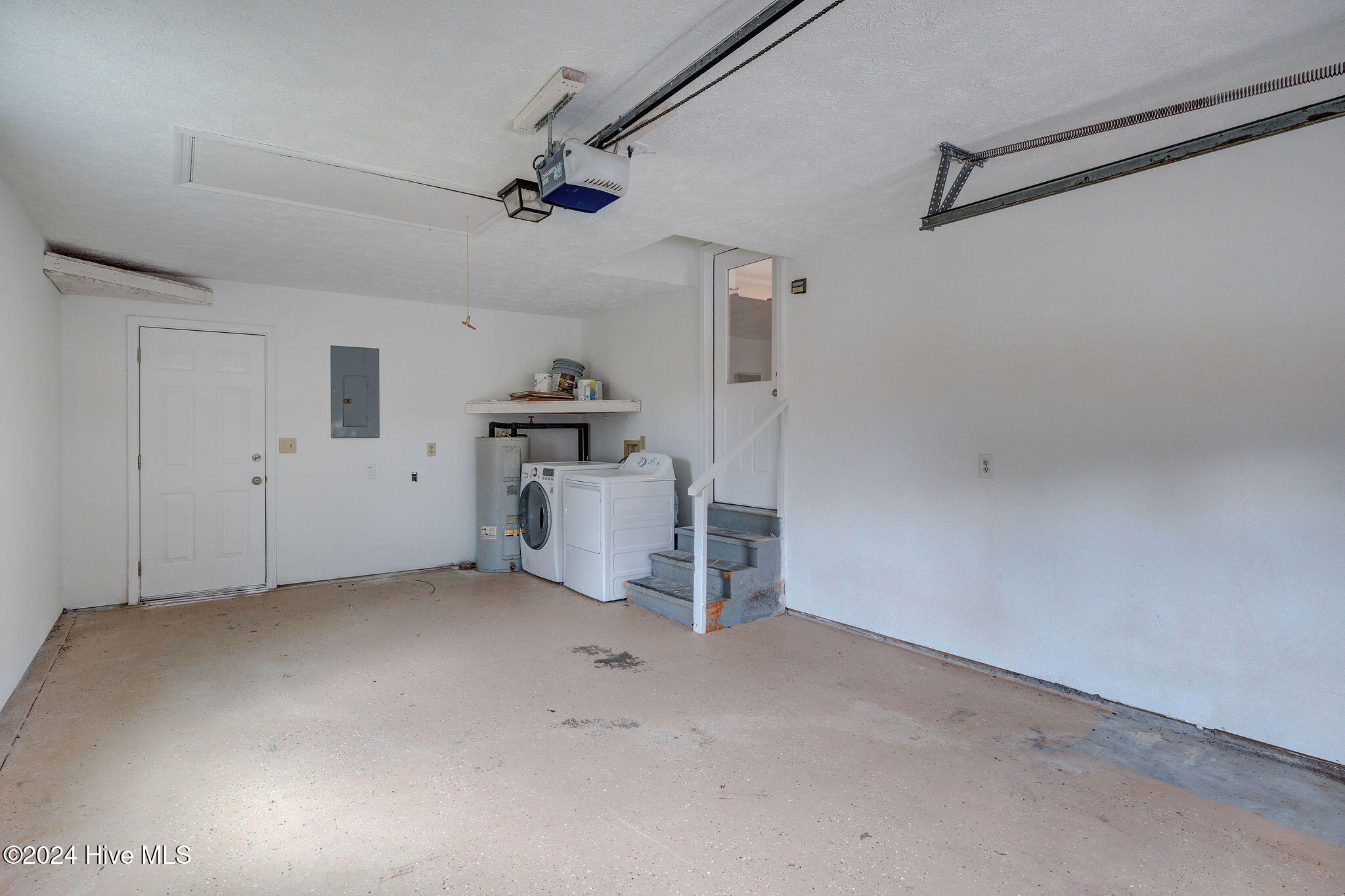 Garage with washer and dryer beside stairs leading to an interior door.