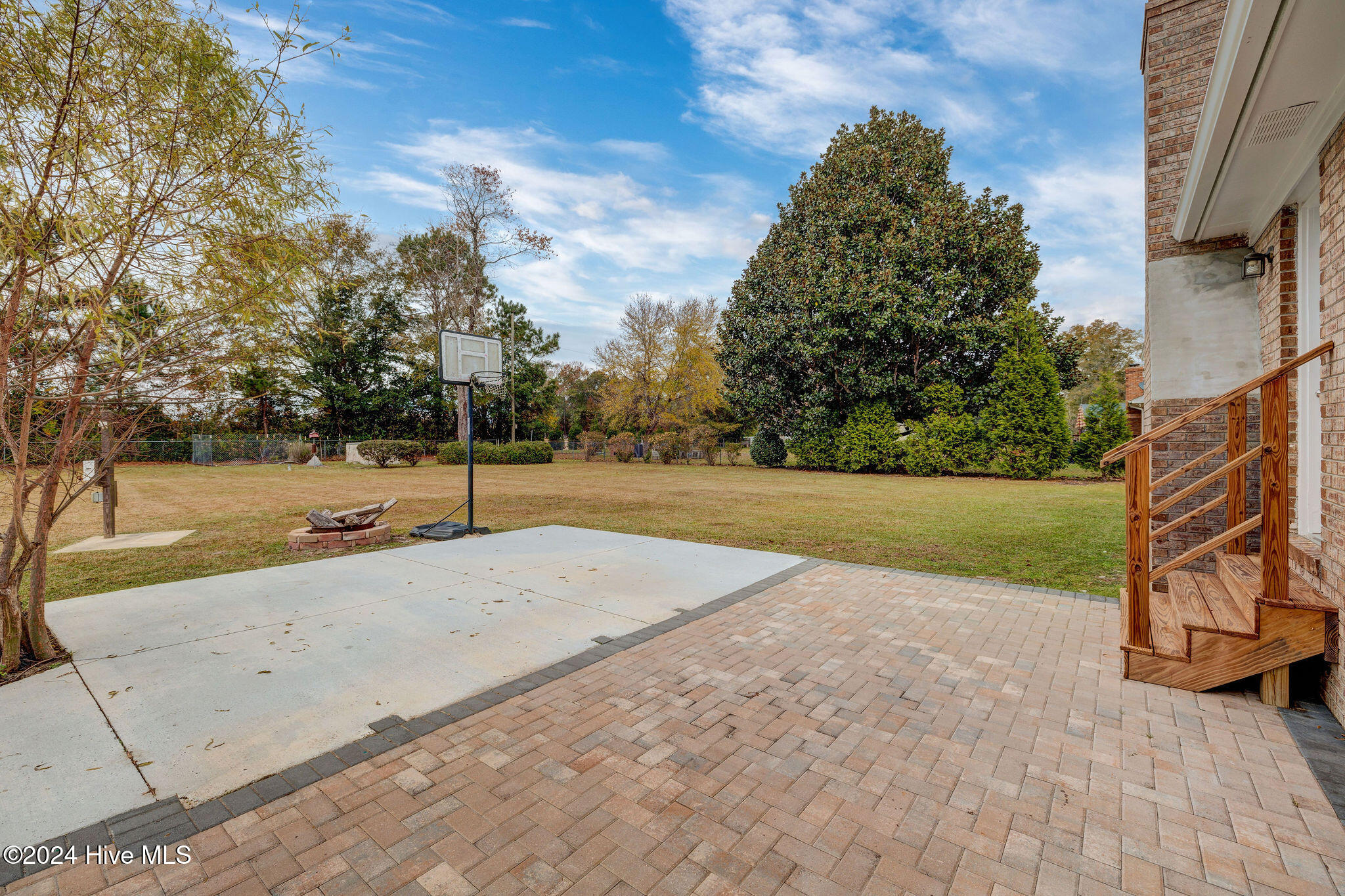 Backyard patio and basketball court with a portable hoop, fire pit, lawn, and wooden house steps.