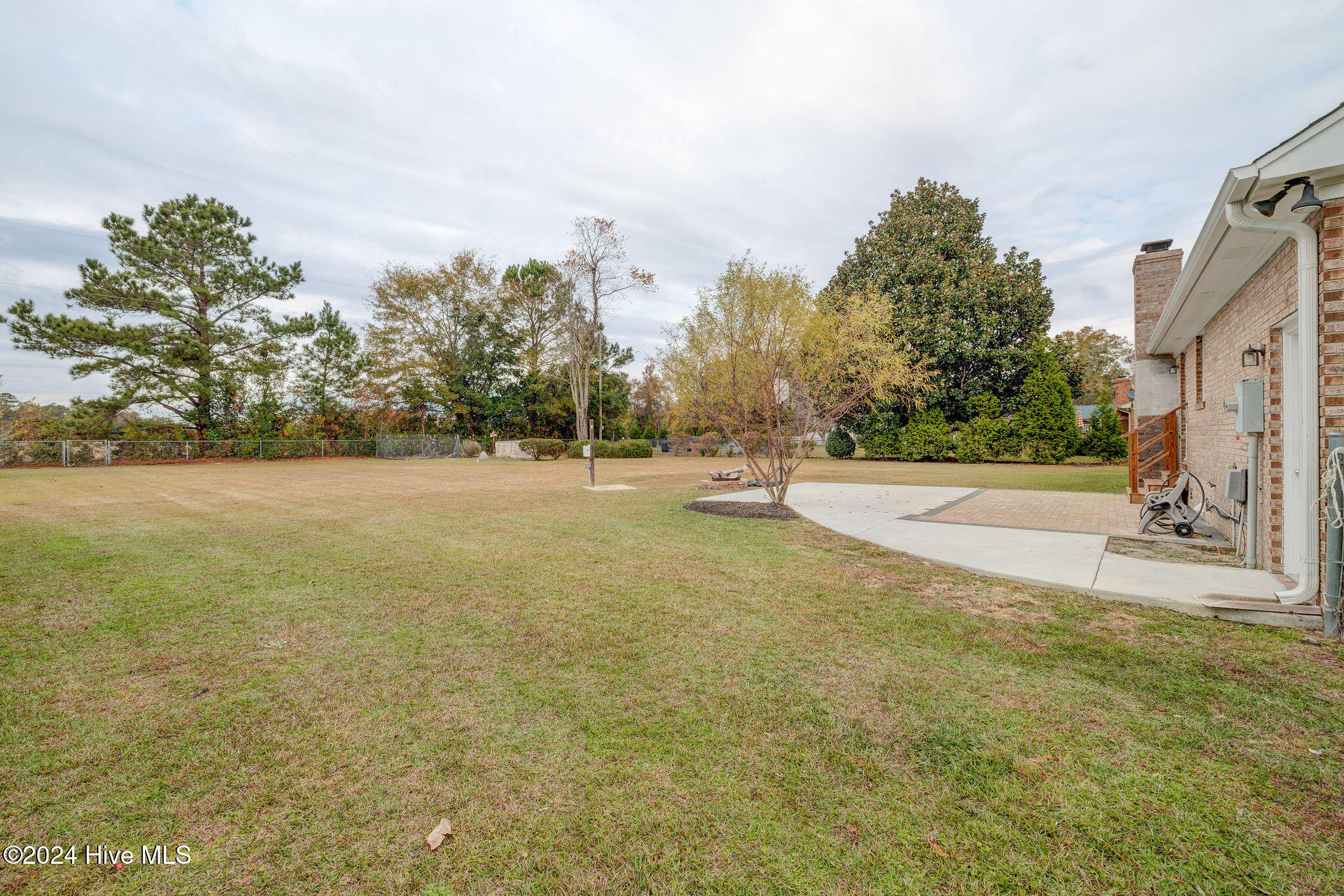 Spacious backyard with a broad lawn, mature trees, and a patio beside the brick house.