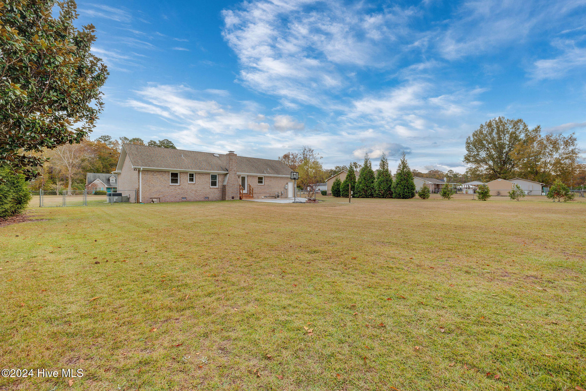Brick home beyond a broad backyard lawn, with a basketball hoop and fenced area.
