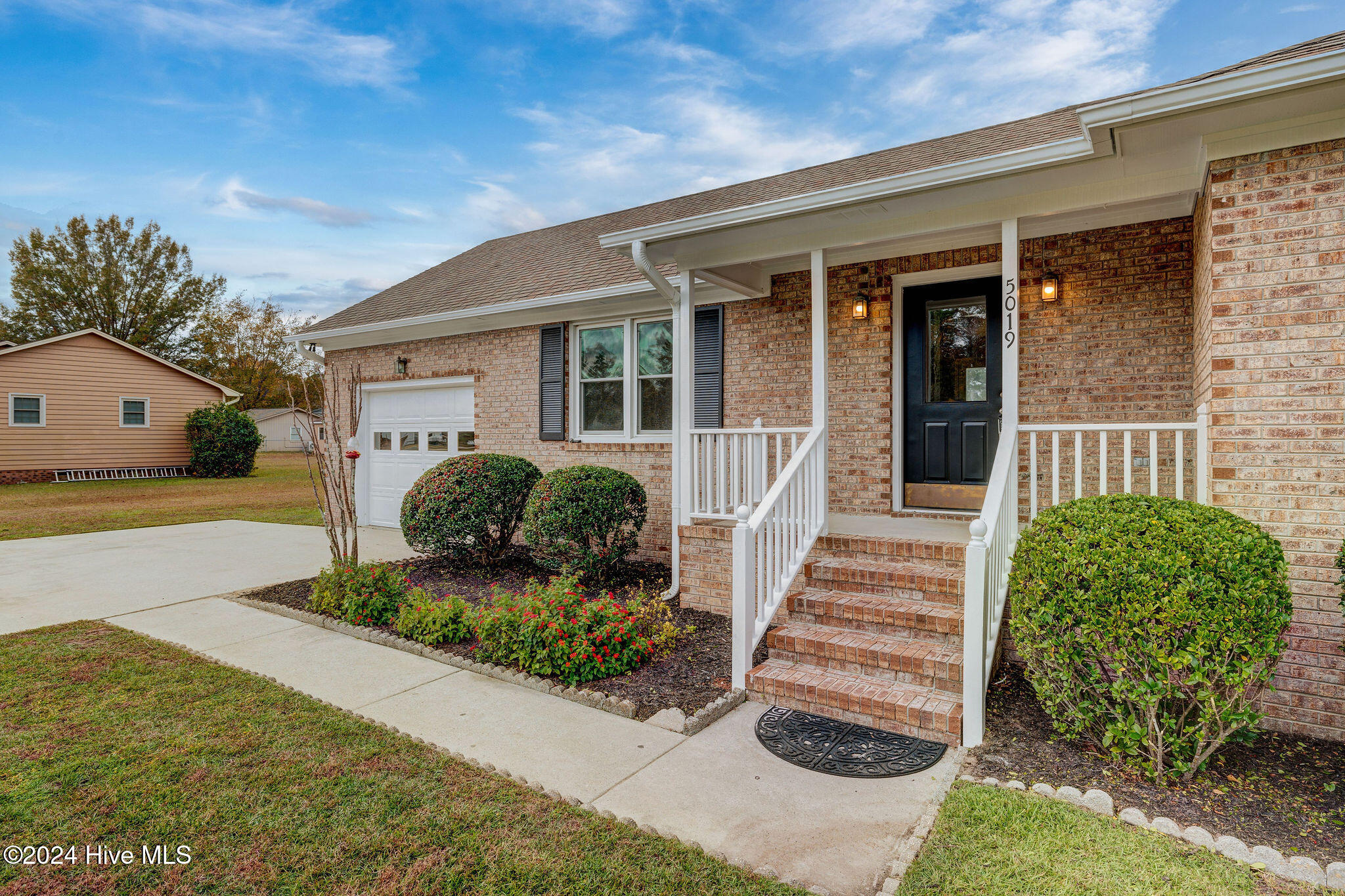 Brick home exterior with a covered porch, brick steps, landscaped entry, and white garage door.