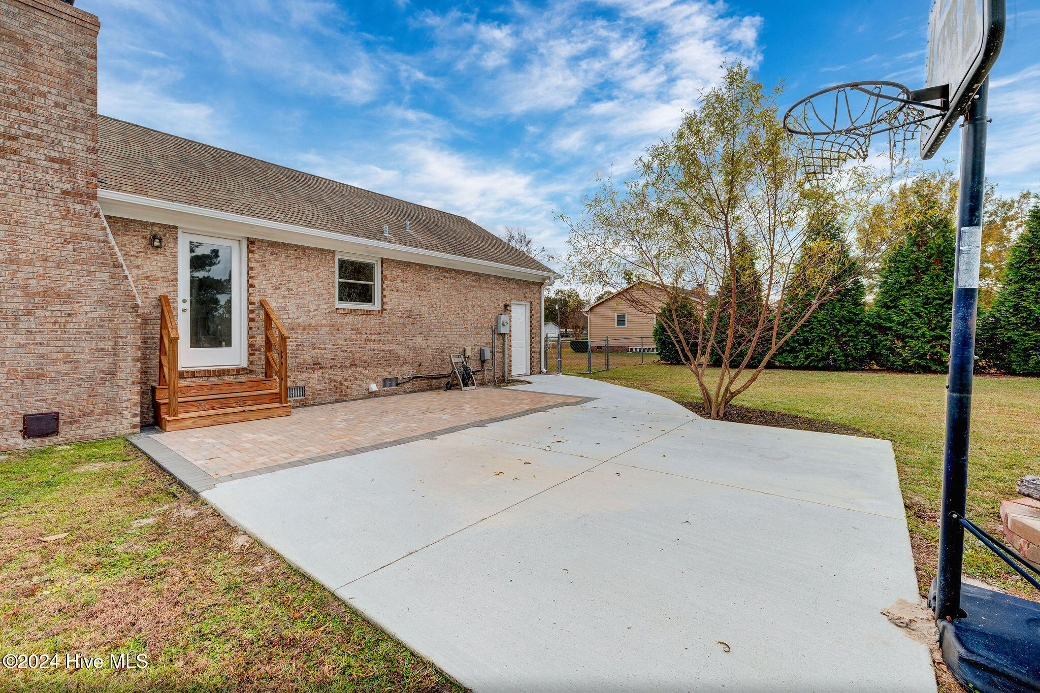Brick home's rear patio with a wooden stoop, broad concrete slab, and basketball hoop.