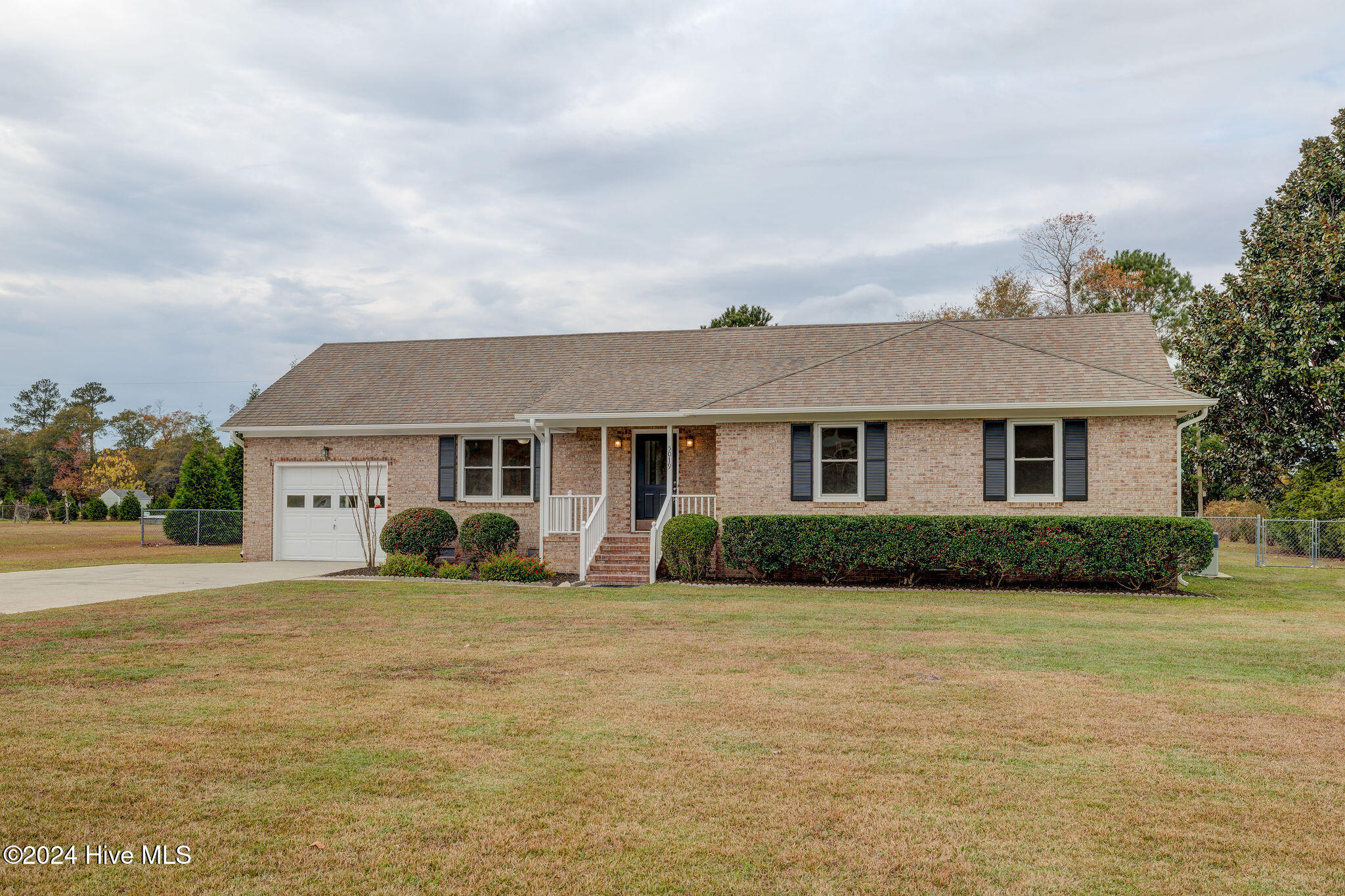Single-story brick ranch home with an attached garage, front steps, clipped hedges, and a broad lawn.