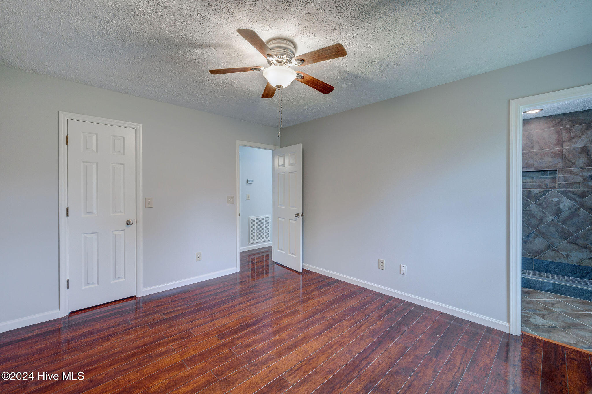 Empty room with glossy wood-look floors, a ceiling fan, and an adjoining tiled bathroom.